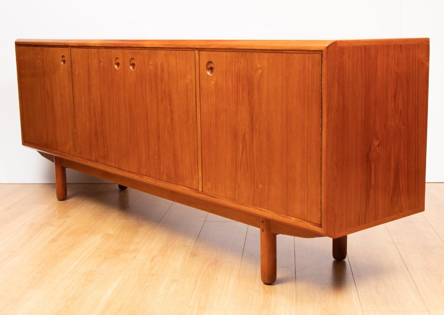A very well made and solid large teak Danish sideboard which features four doors with feature recessed turned handles. The sideboard sits on four solid Teak turned legs. The left hand cupboard is split in two vertically with a storage space on the