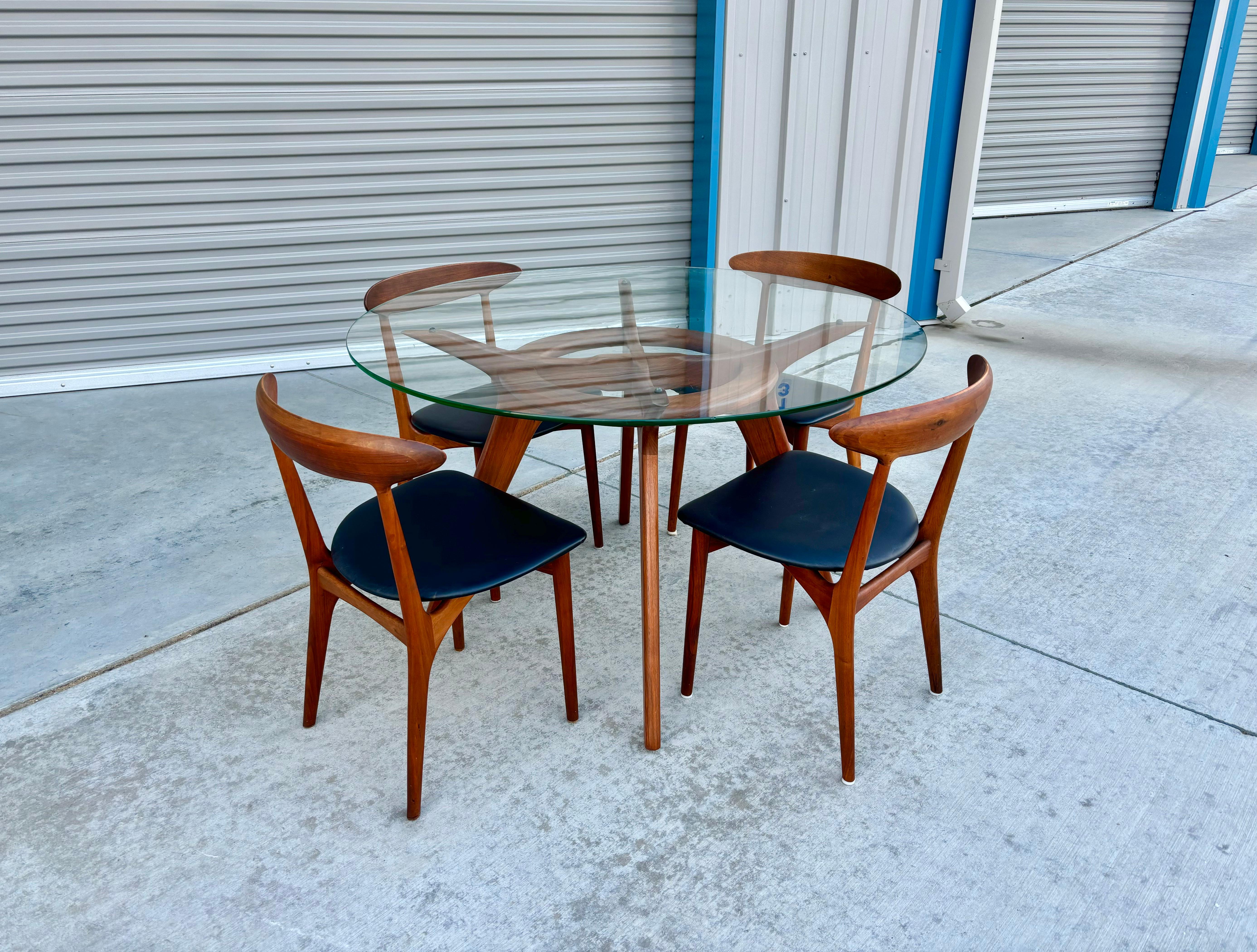 This beautiful dining room set features four teak chairs designed by Kurt Ostervig and manufactured by Brande Møbelindustri. The set also has a round glass top that gracefully sits on a solid walnut base. They were designed by Adrian Pearsall and