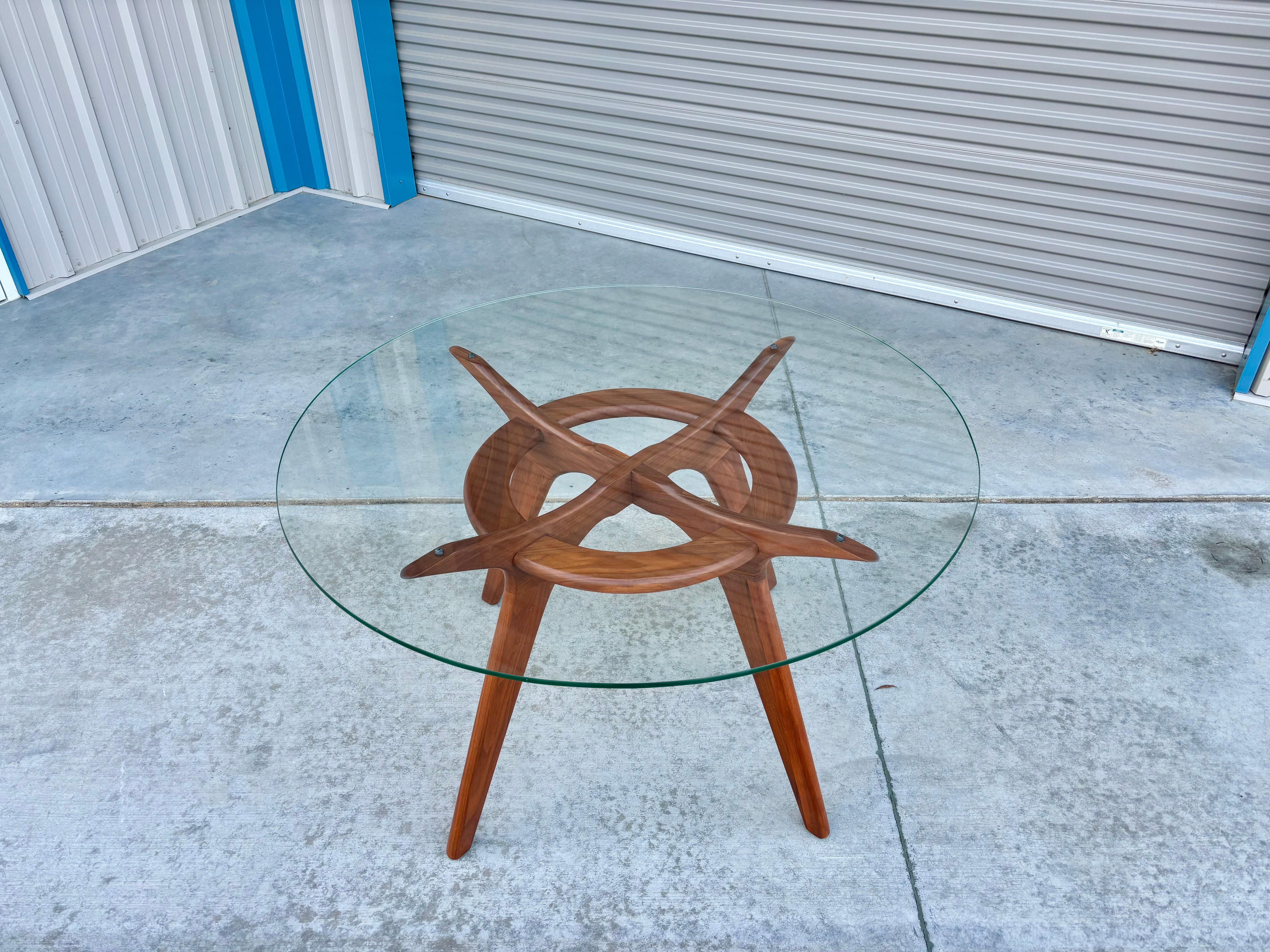 This stunning dining table is a true masterpiece of mid-century design, crafted by the renowned Adrian Pearsall and produced by Craft Associates. The table's exquisite circular glass top is elegantly supported by a sturdy walnut frame base,