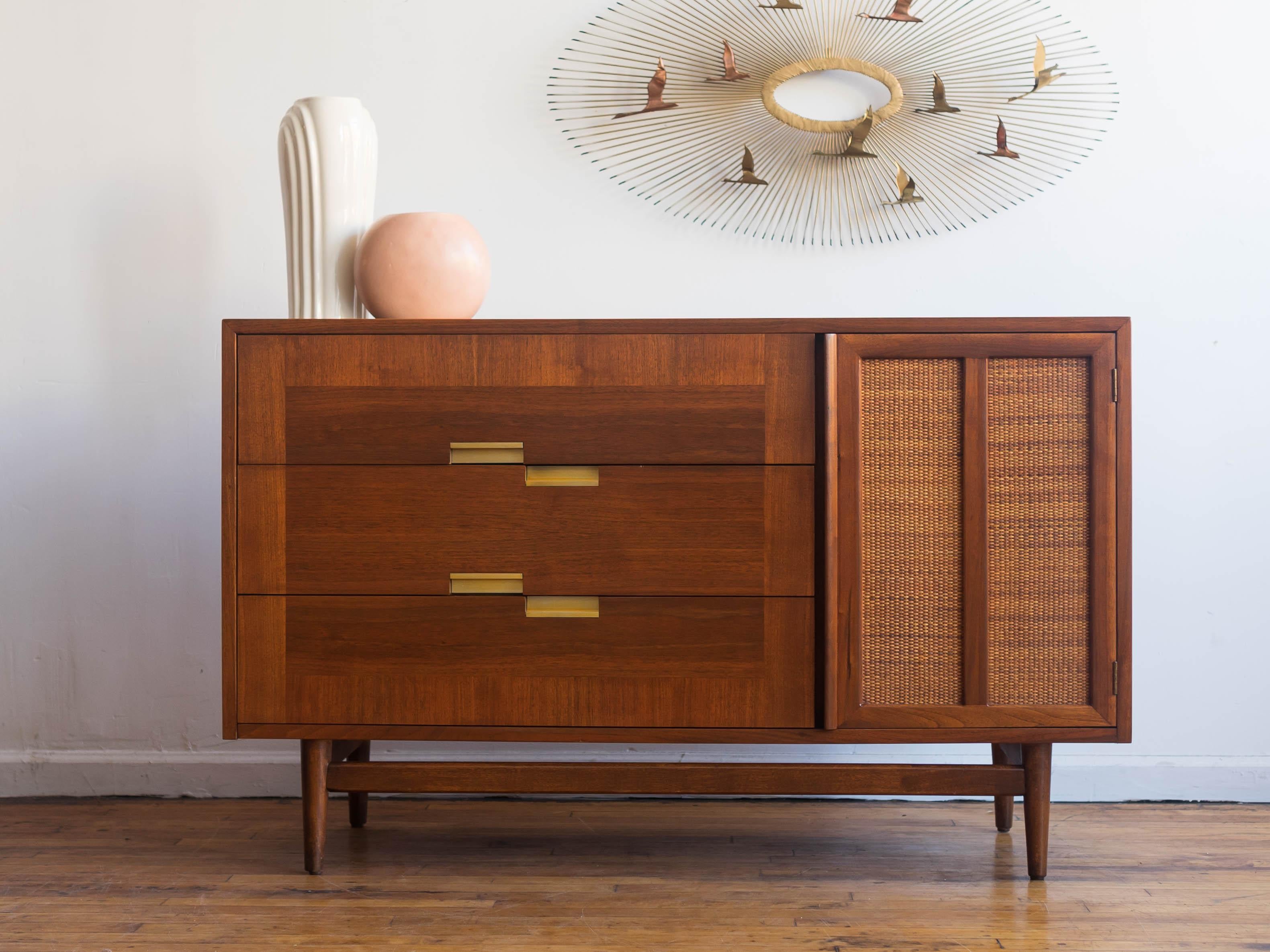 Measures: 50” x 18.5” x 31”H

American of Martinsville Accord credenza in walnut with three drawers one one cane-front door. Warm walnut woodgrain with a contrasting border around the drawers and the line's signature gold-toned hardware and