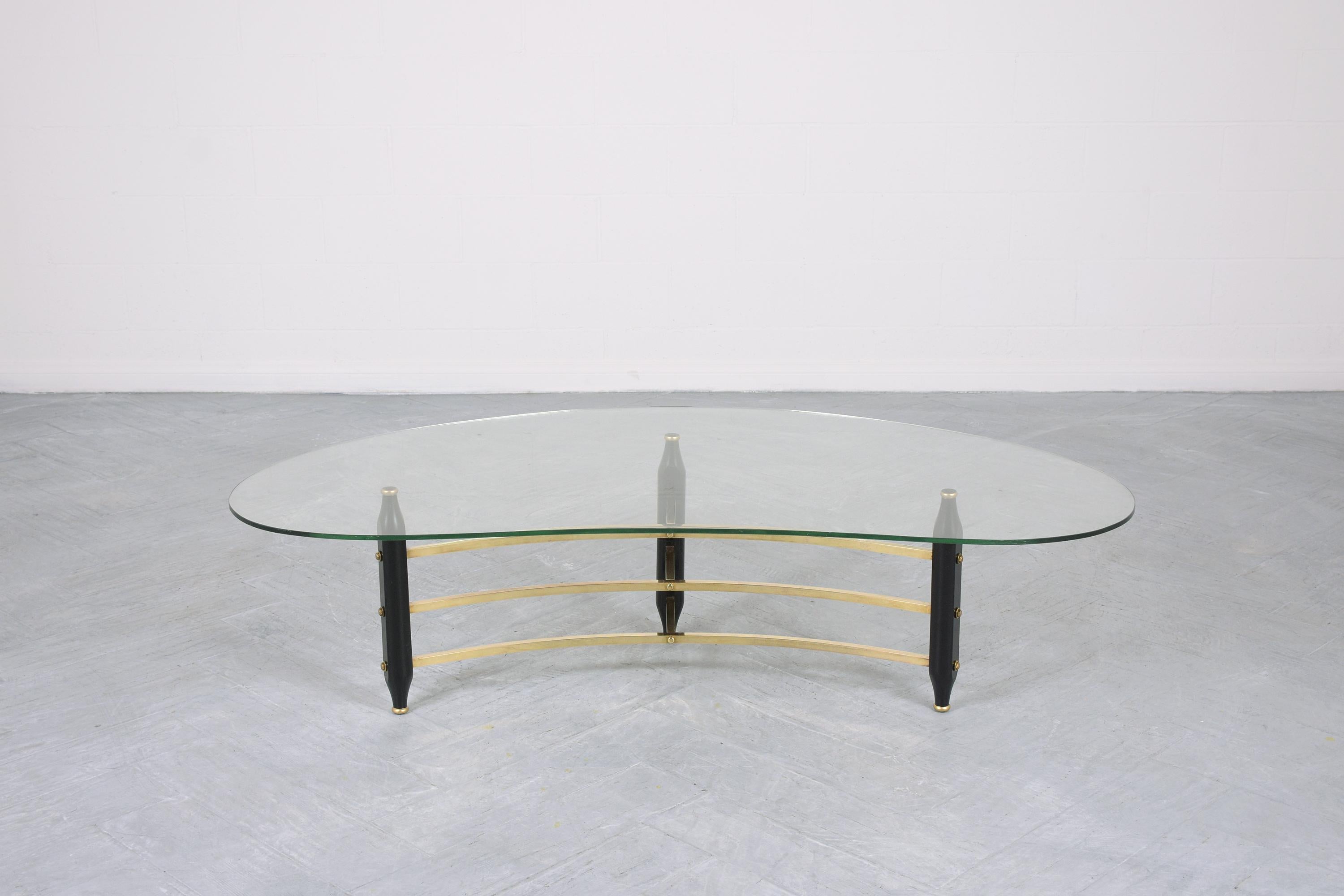 This 1960s Mid-Century Modern brass glass top coffee table has a base crafted out of a wood & brass combination and has been completely restored by our team of expert craftsmen. The table comes with a new kidney-shaped 3/8 inches thick glass top