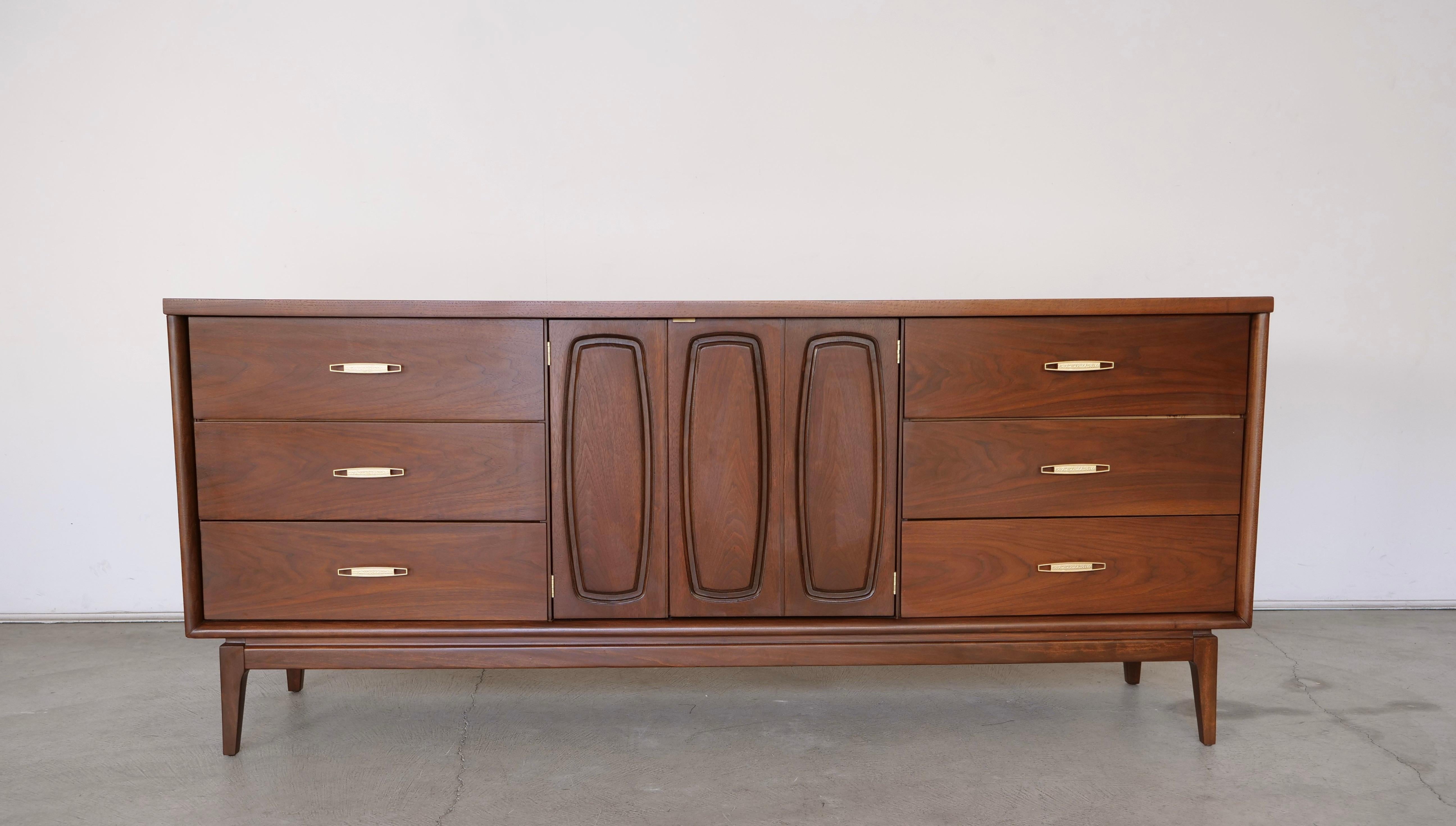 The Broyhill Emphasis dresser is a midcentury modern piece in walnut by the Broyhill Furniture Company in the 1960s. It has been professionally refinished, with the original handles and hardware restored. It is part of the Emphasis line. The dresser