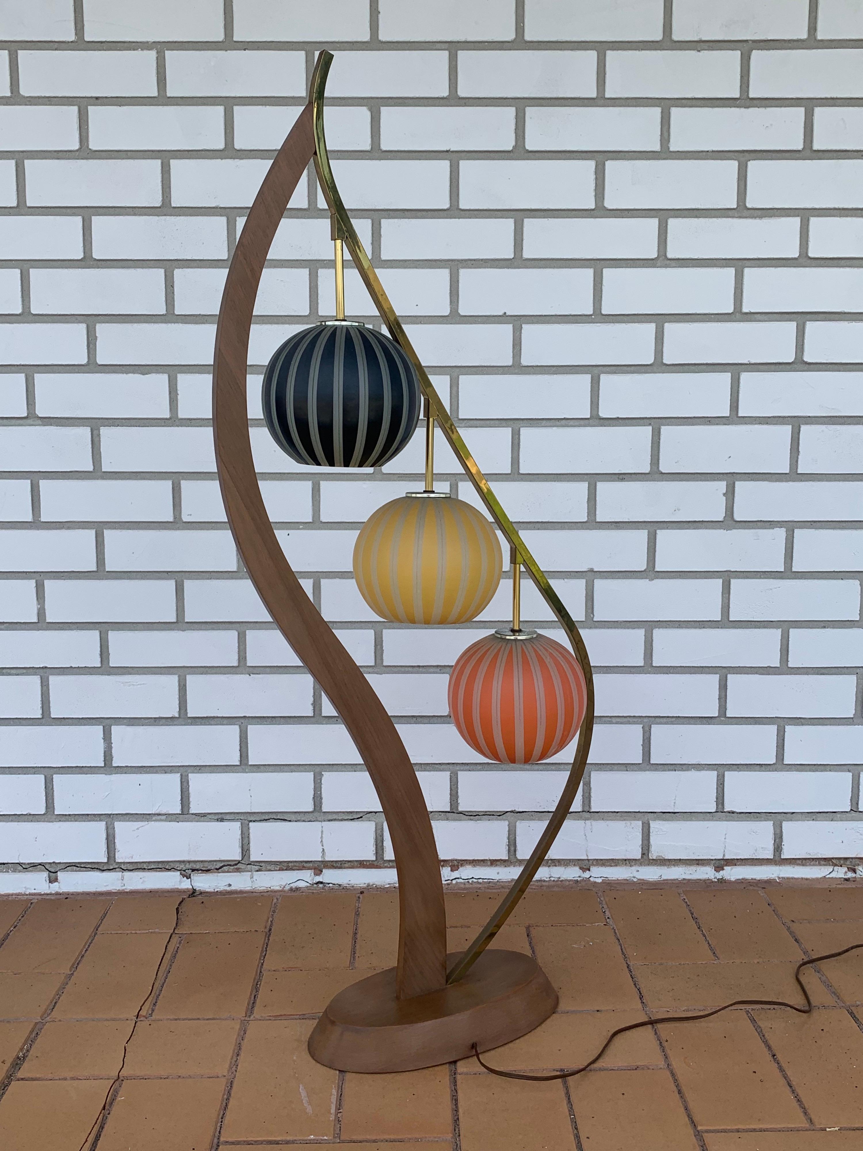 Mid-Century Modern floor lamp. Has a beautiful harp shape in wood and brass. 3 globes in Blue, Yellow and Red. Each turn of the light switch will turn on a different number of bulbs from 1 to 2 to 3 then off to offer a variety of lighting options.