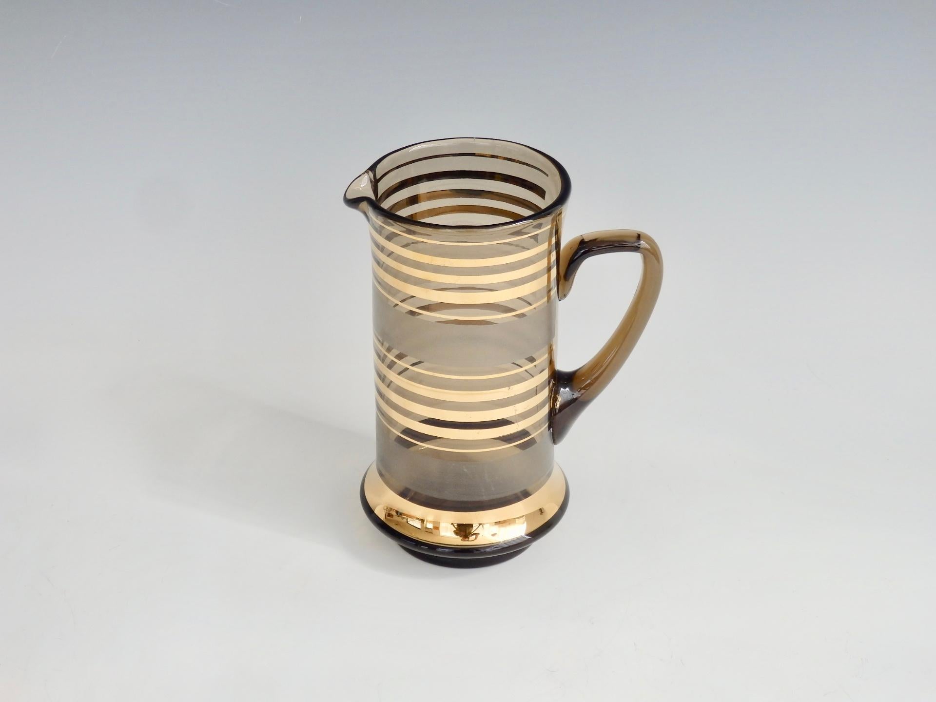 A 1960s Mid-Century Modern gold stripe glass cocktail pitcher. This is a gem of a cocktail pitcher with rich gold cylindrical striping and frosted bands on smoke glass, finished with a polished bottom. A tasteful vintage addition to any bar or