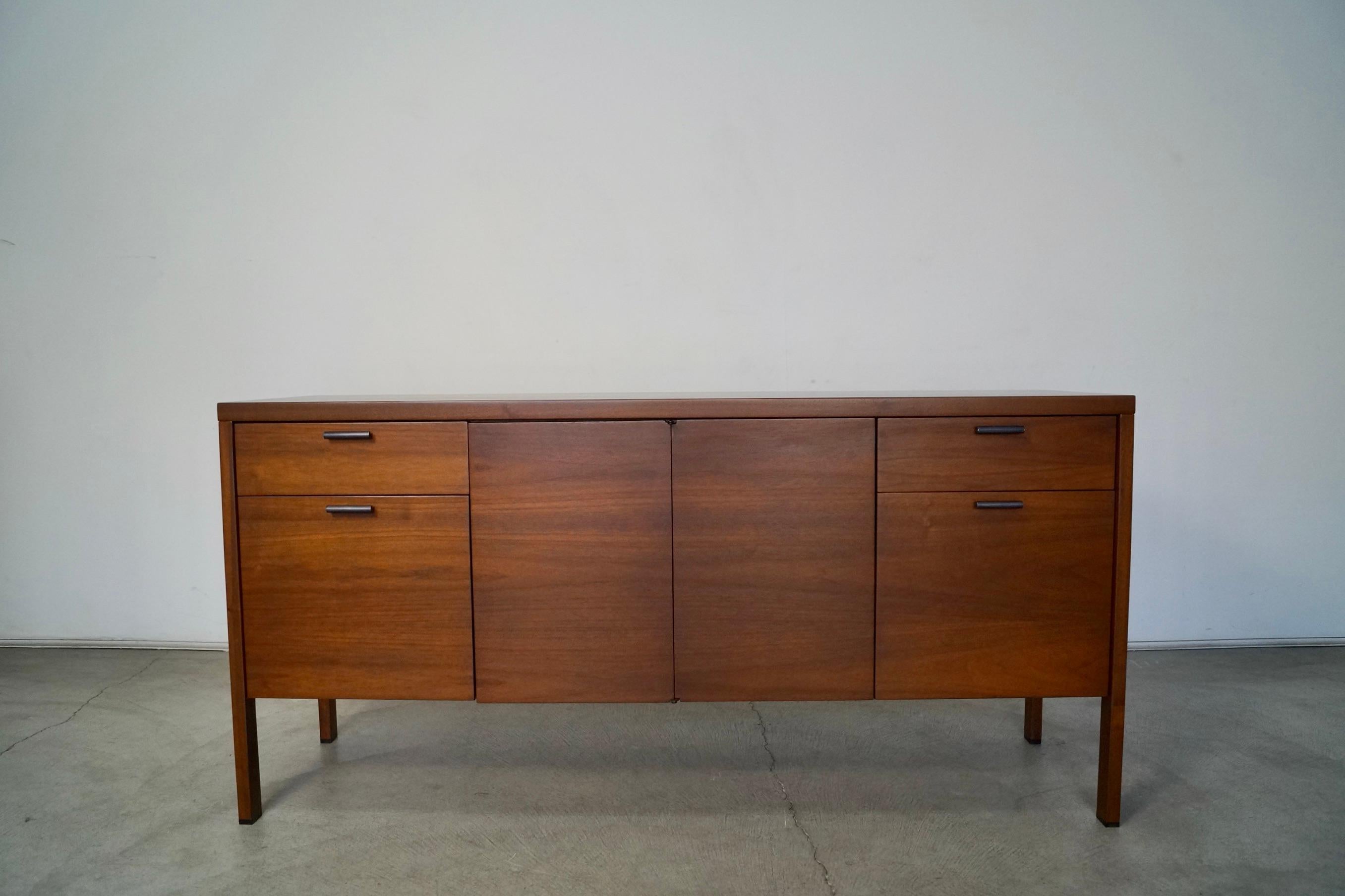 Vintage 1960s Mid-Century Modern credenza for sale. Made of walnut, and has been professionally refinished. It has four drawers, and a bi-folding door that opens up to a shelf that is adjustable. It has the original black metal hardware with black