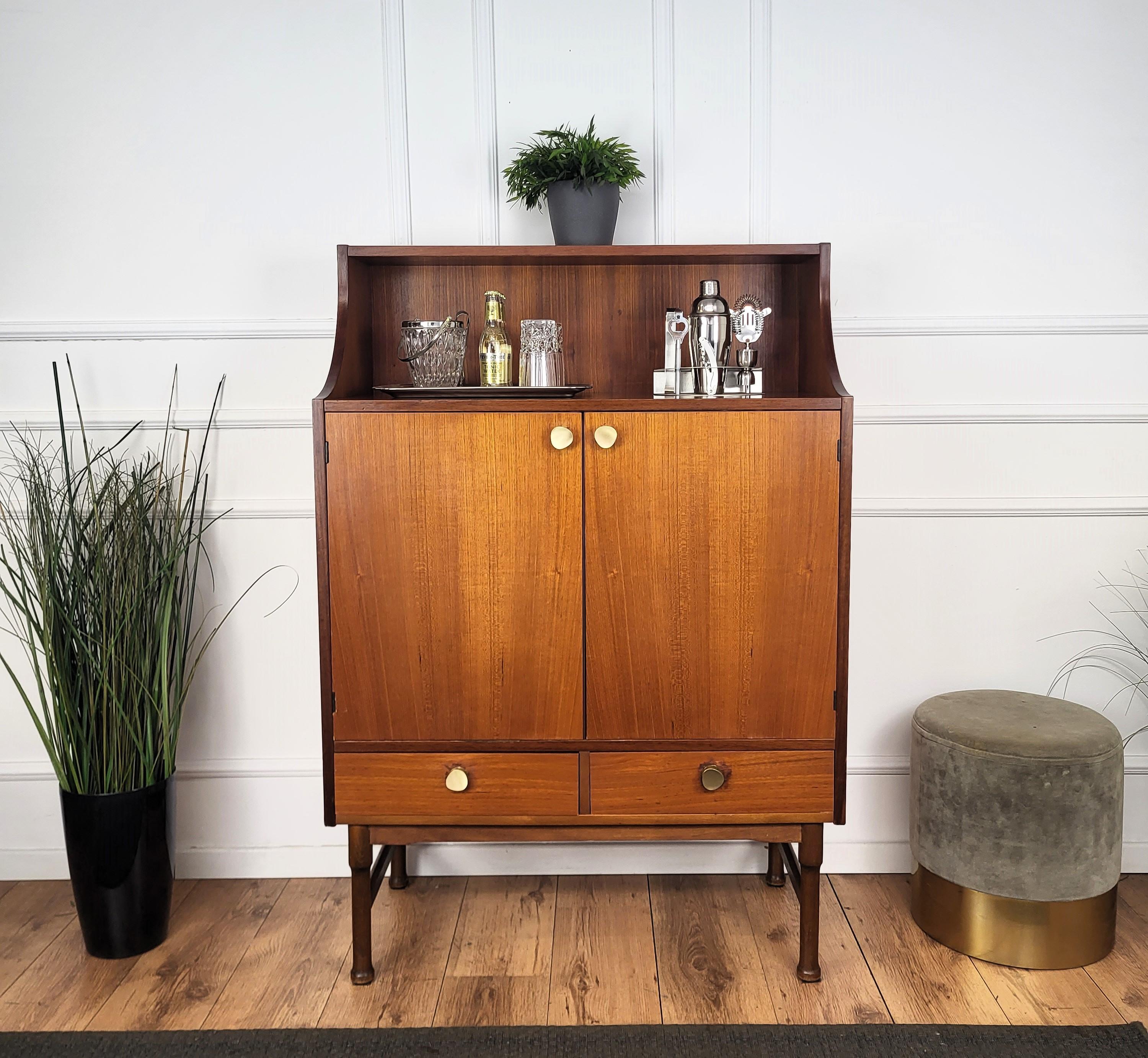 Very elegant Italian Mid-Century Modern dry bar cocktail cabinet, in beautiful wood with top shelves, central doors with internal storage, two bottom drawers all highlighted by the brass handes and standing on typical carved Italian Mid-Century
