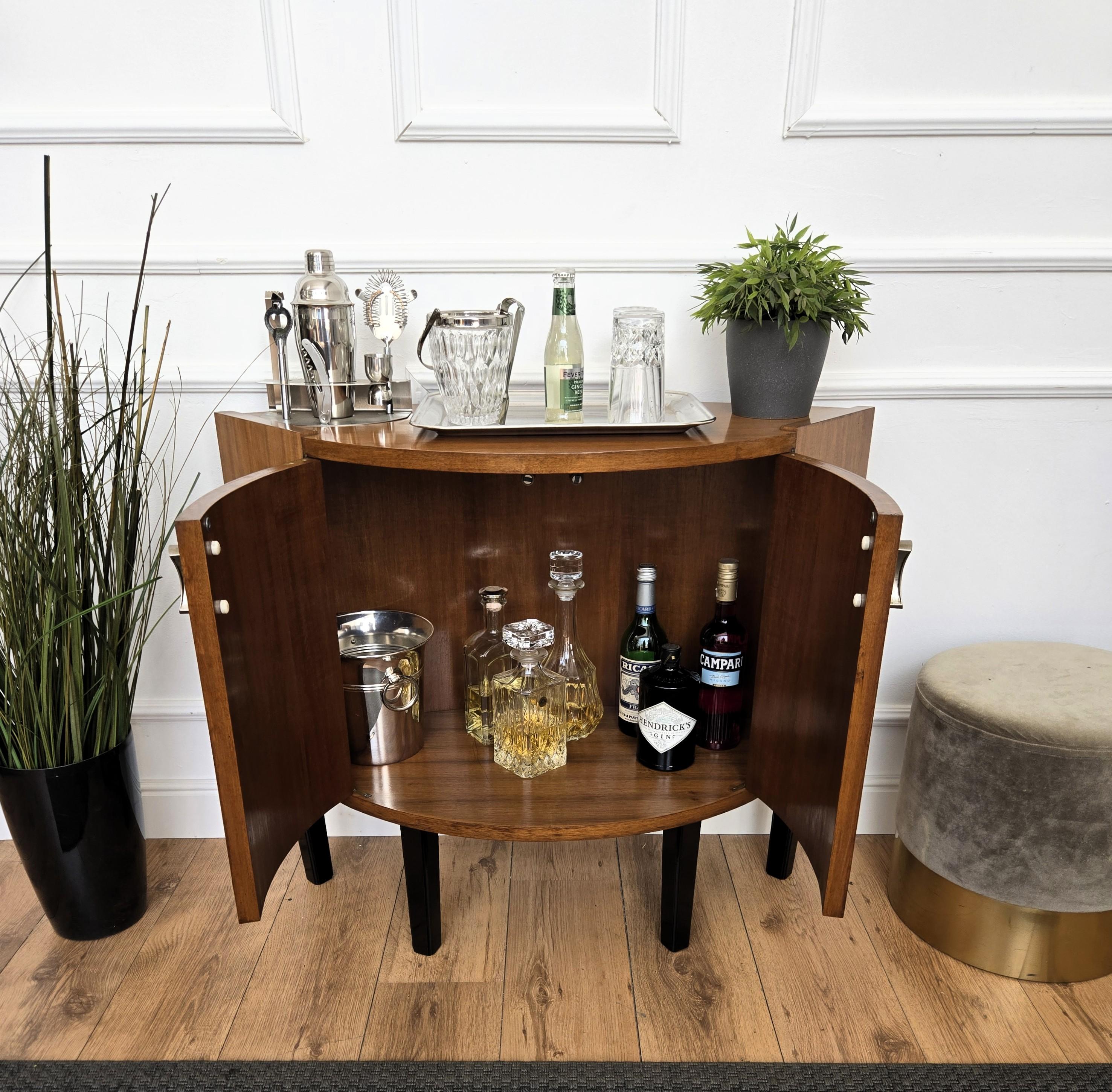 Elegante mueble bar italiano de mediados de siglo, en madera noble, con puertas centrales y tiradores de latón, realzado por el lateral de diseño y forma típicos de mediados de siglo y apoyado sobre cuatro patas negras. Su diseño único y