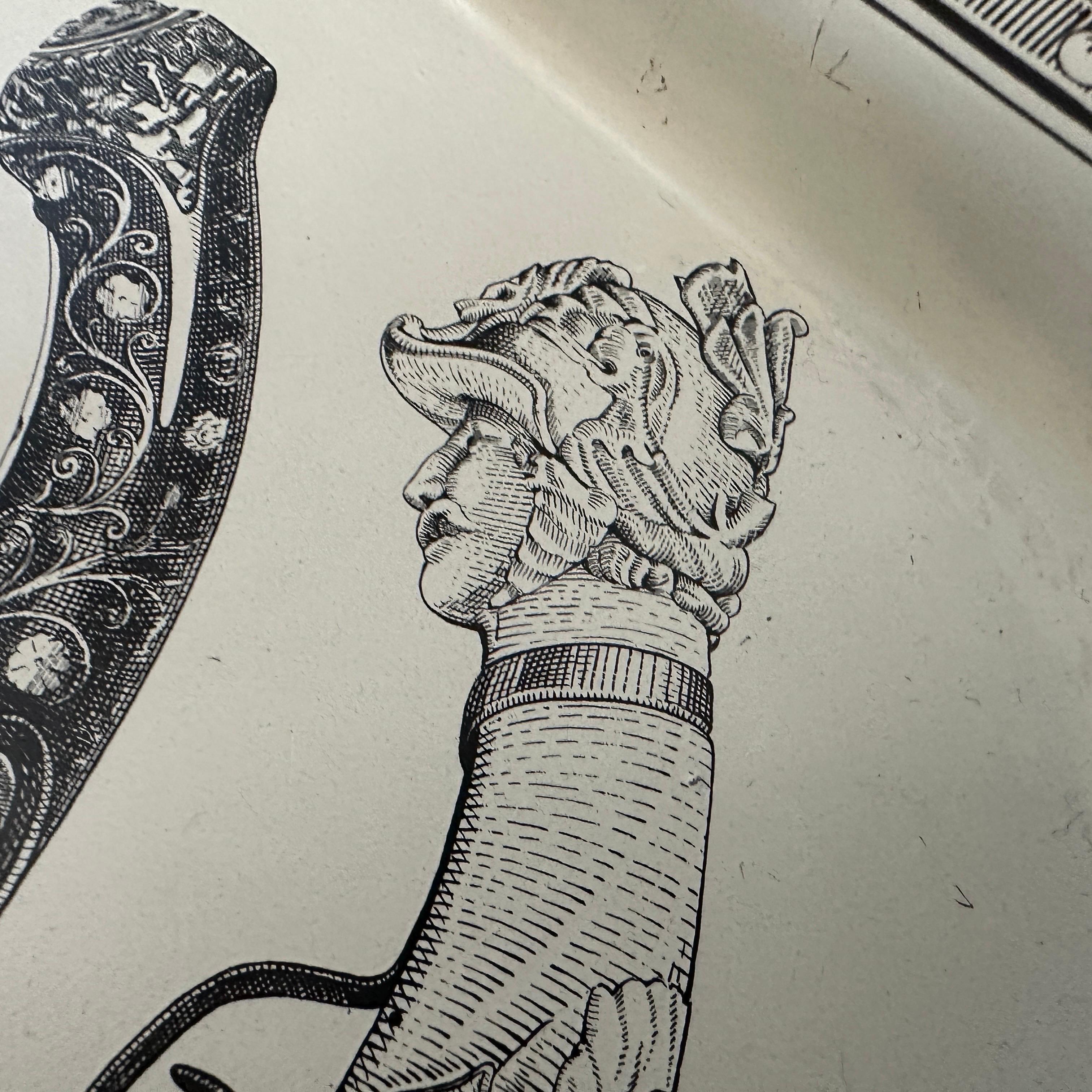 This Fornasetti tray is a striking example of the brand’s signature artistic and surrealist aesthetic. 
The tray is made of metal with a enameled finish that provides a smooth surface, characteristic of Fornasetti’s craftsmanship. The tray features