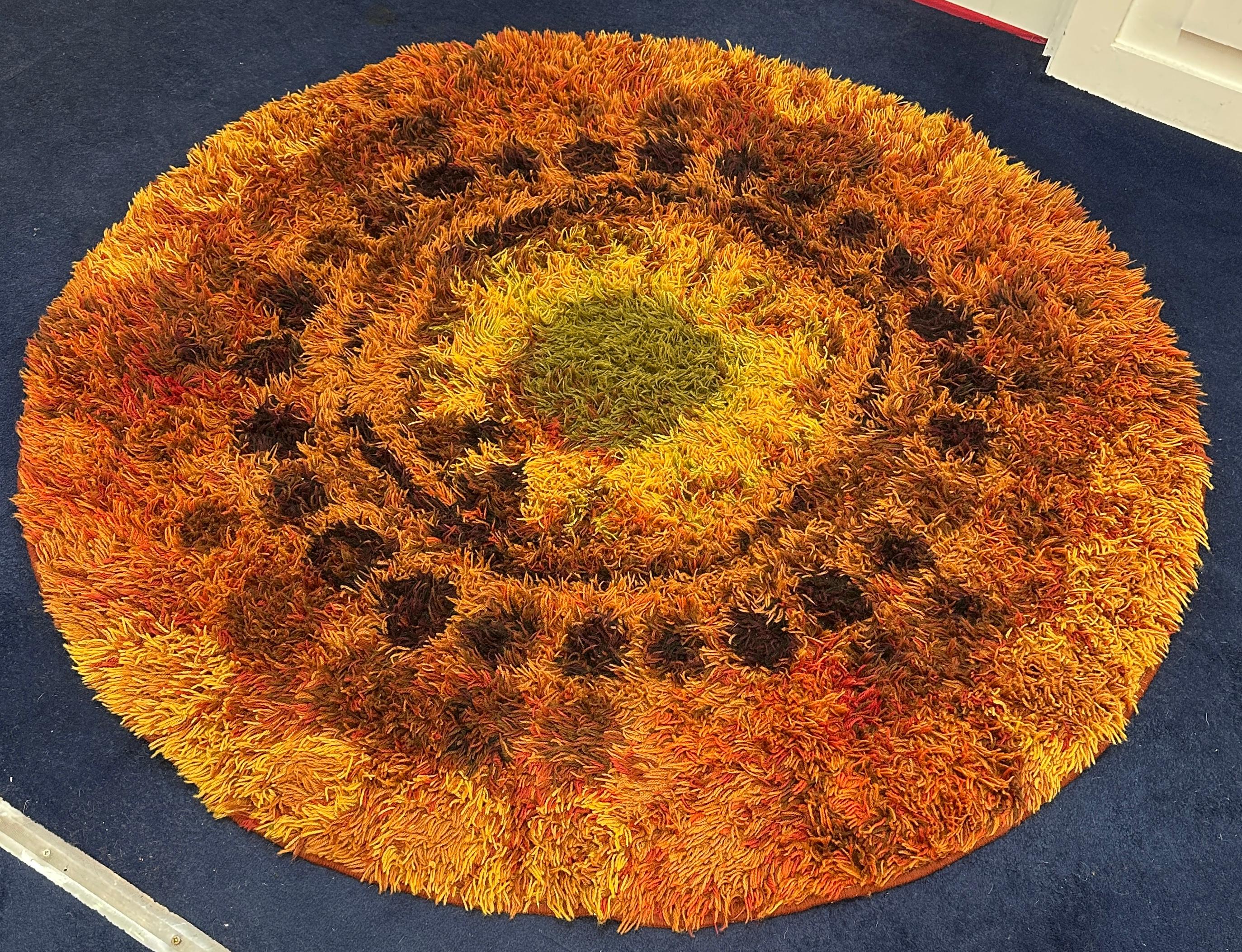 1960s mid century modern retro English shagpile rya rug.  Made from nylon and wool in different shades of orange, green, yellow and brown.  A green sun design with yellow abstract flames is woven into the centre of the rug with a number of brown