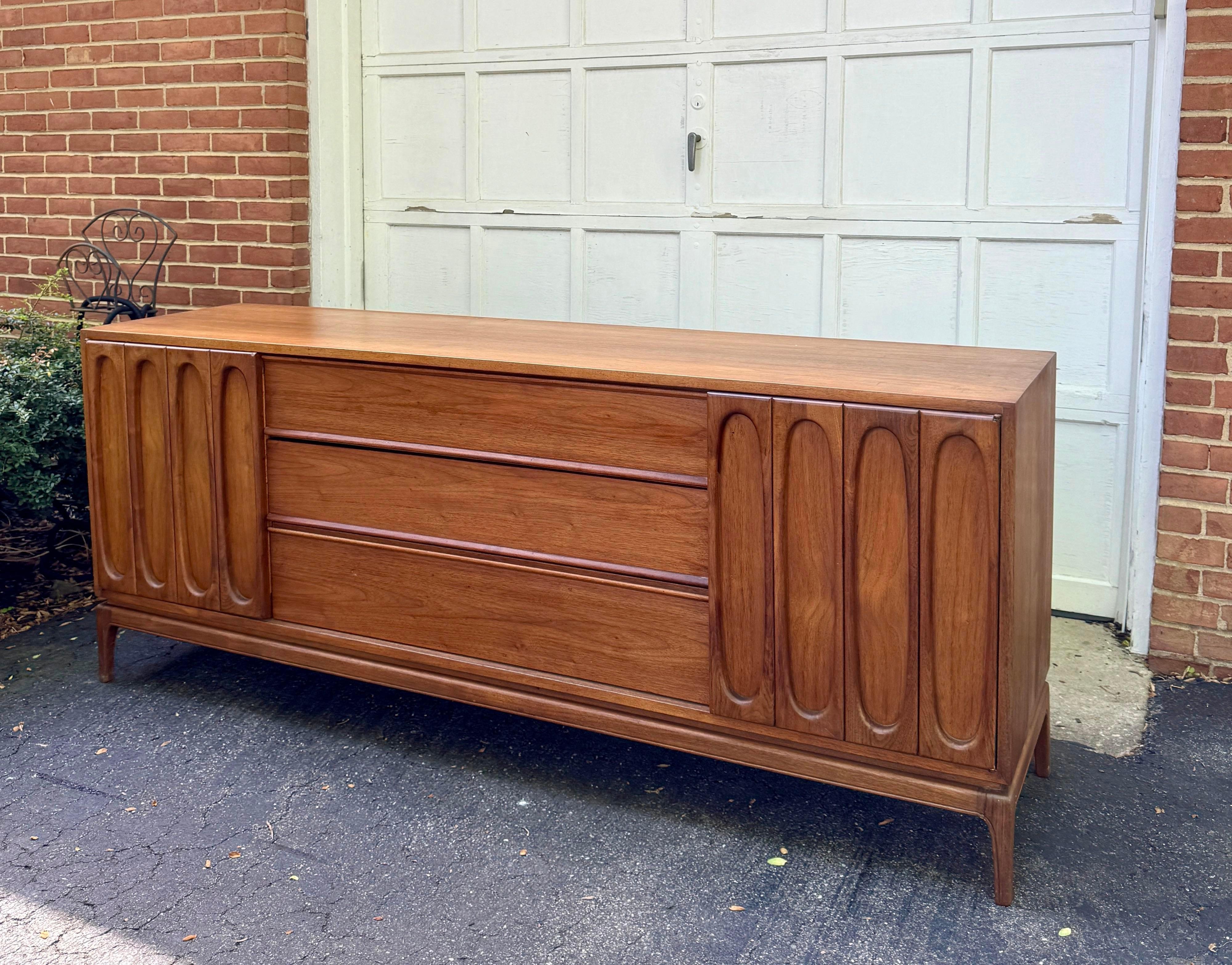 Gorgeous sculptural walnut dresser featuring a stunning sculptural design, adorned with three spacious central drawers complemented by three smaller drawers concealed behind elegantly crafted doors on each side. 

