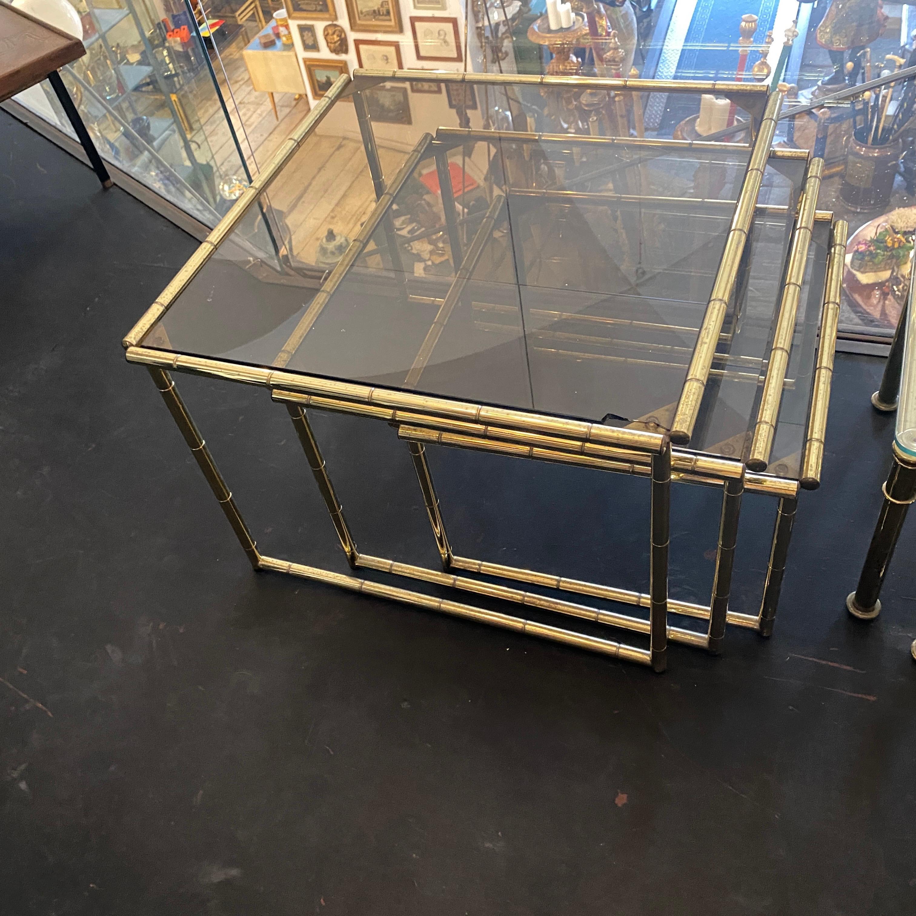 Three brass and smoked glass nesting tables designed and manufactured in Italy in the Sixties in the manner of Tommaso Barbi. Brass it's in original patina, glasses have signs of use and age visibles in the photos. Italian design during the mid-20th