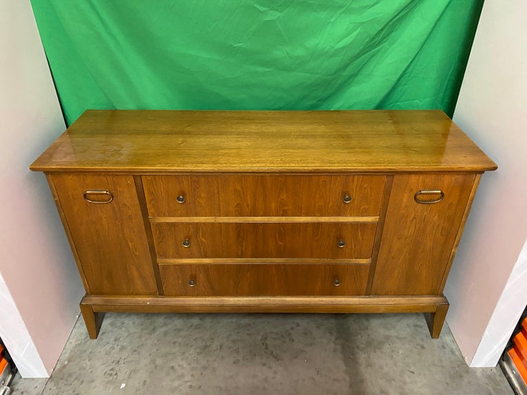 1960s Mid-Century Modern teak sideboard. Teak sideboard with three drawers at center flanked by cabinet doors at either end. Top drawer has divided and lined section for silverware.