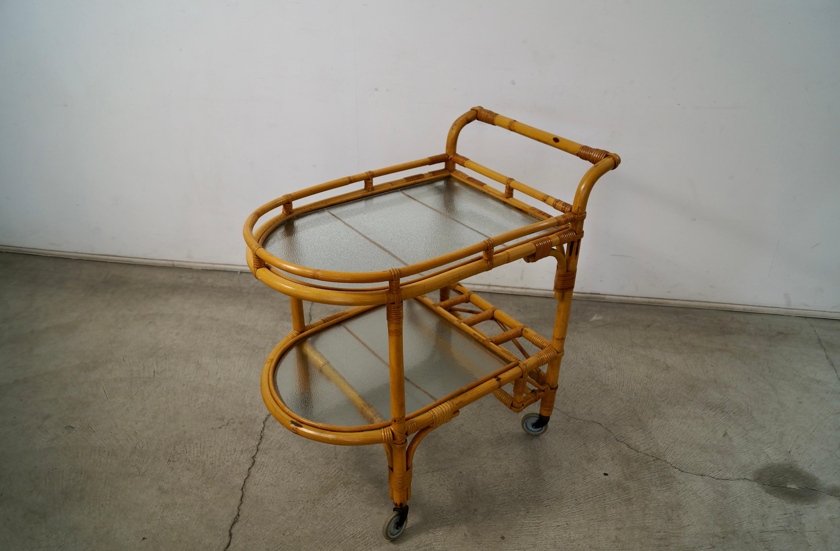 Carrello da bar in rattan vintage del Midcentury Modern in vendita. Prodotto negli anni '60 e in ottime condizioni. Ha due ripiani in vetro con una texture anni '60 e una solida struttura in rattan e vimini. Dispone di quattro spazi per le bottiglie