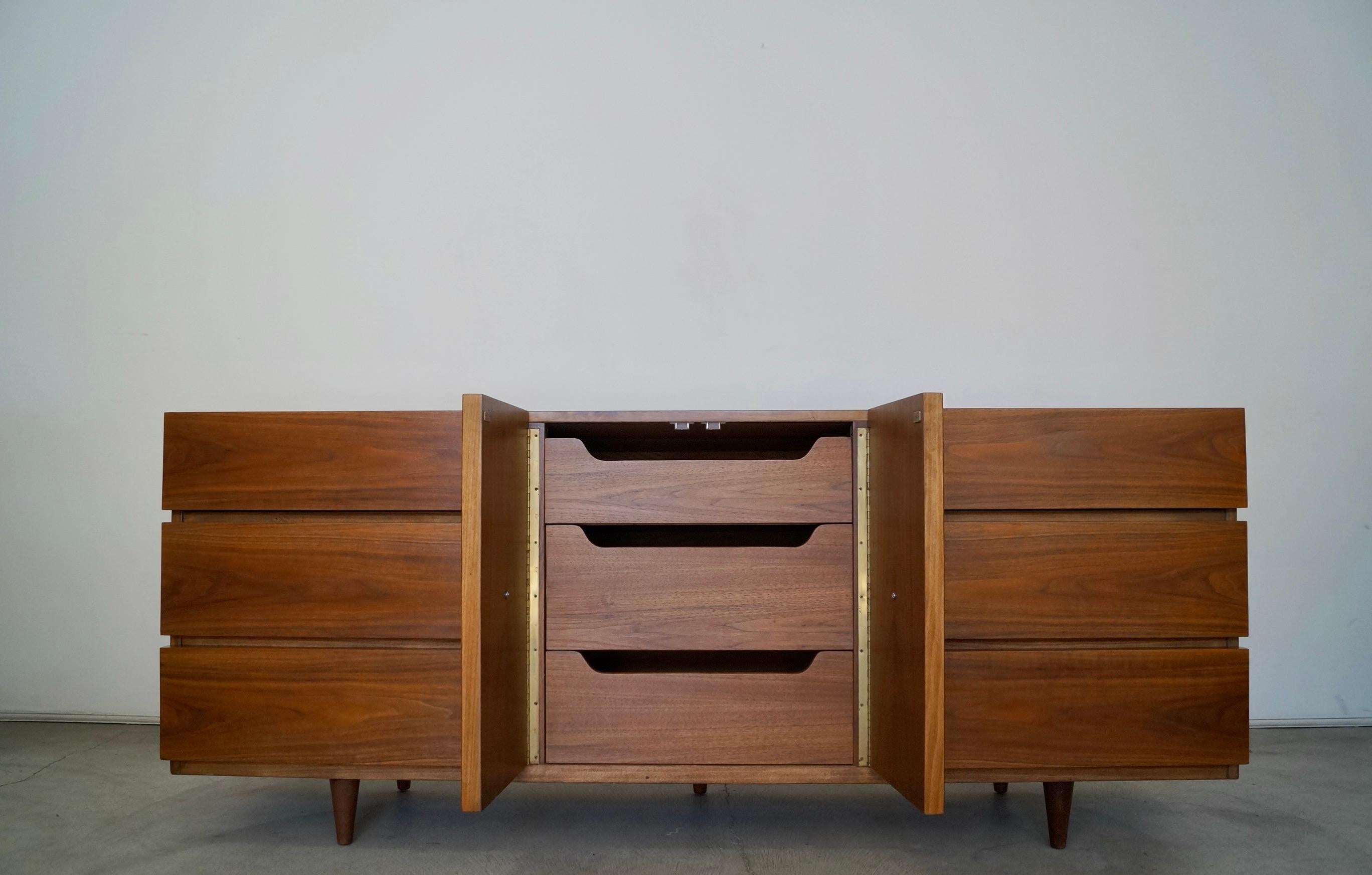 Vintage Mid-Century Modern lowboy dresser / credenza for sale. Manufactured by American of Martinsville, and has been professionally refinished. It's made of walnut, and has beautiful walnut grain throughout. The middle credenza cabinet doors open