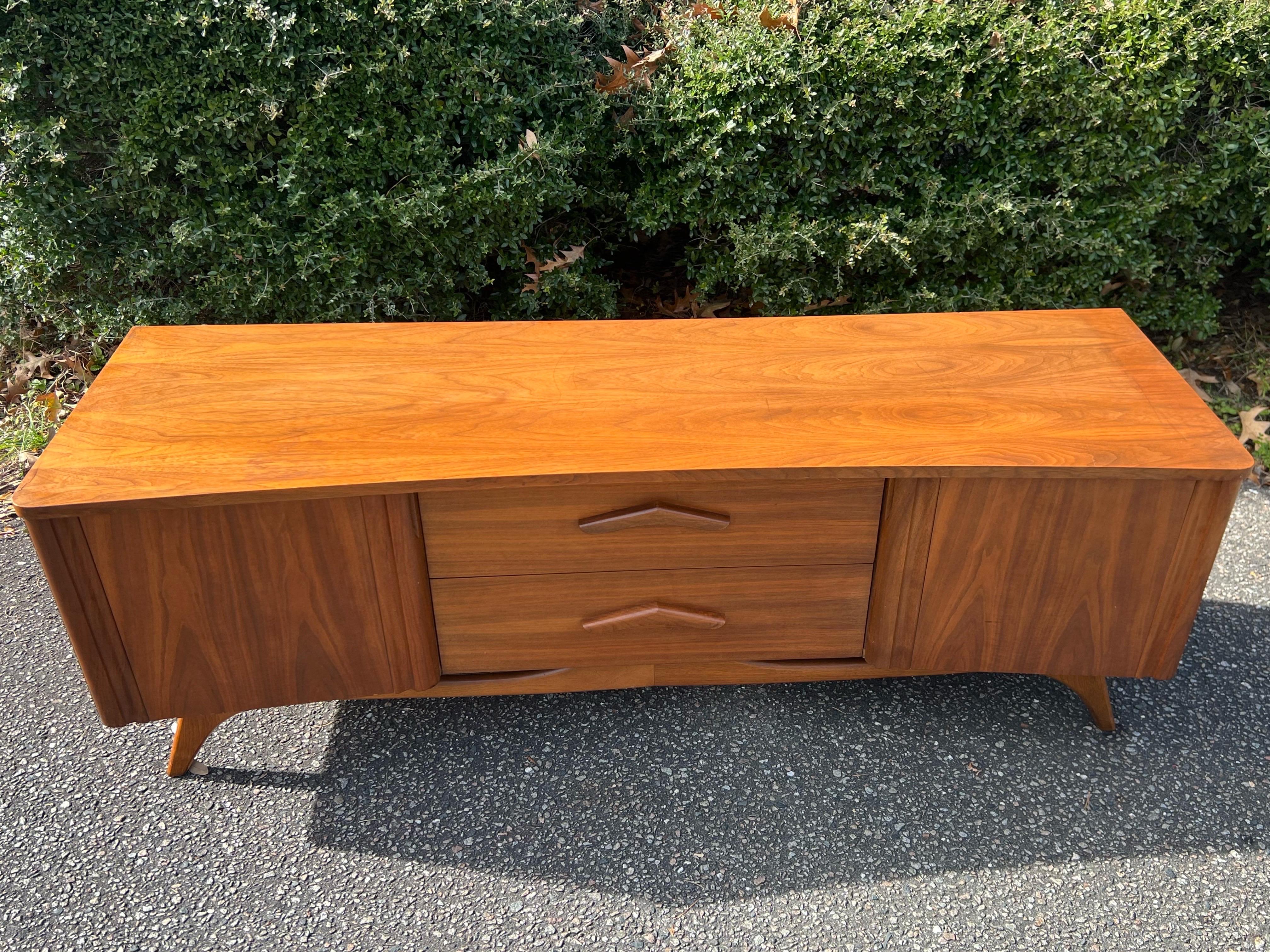 Impressive curved ‘boomerang’ walnut dresser by Young Manufacturing Co.

Features

✨3 large central sliding drawers
✨two opening cabinet doors on both sides with lots of room for storage
✨carved wooden boomerang shaped drawer pulls
✨curvilinear