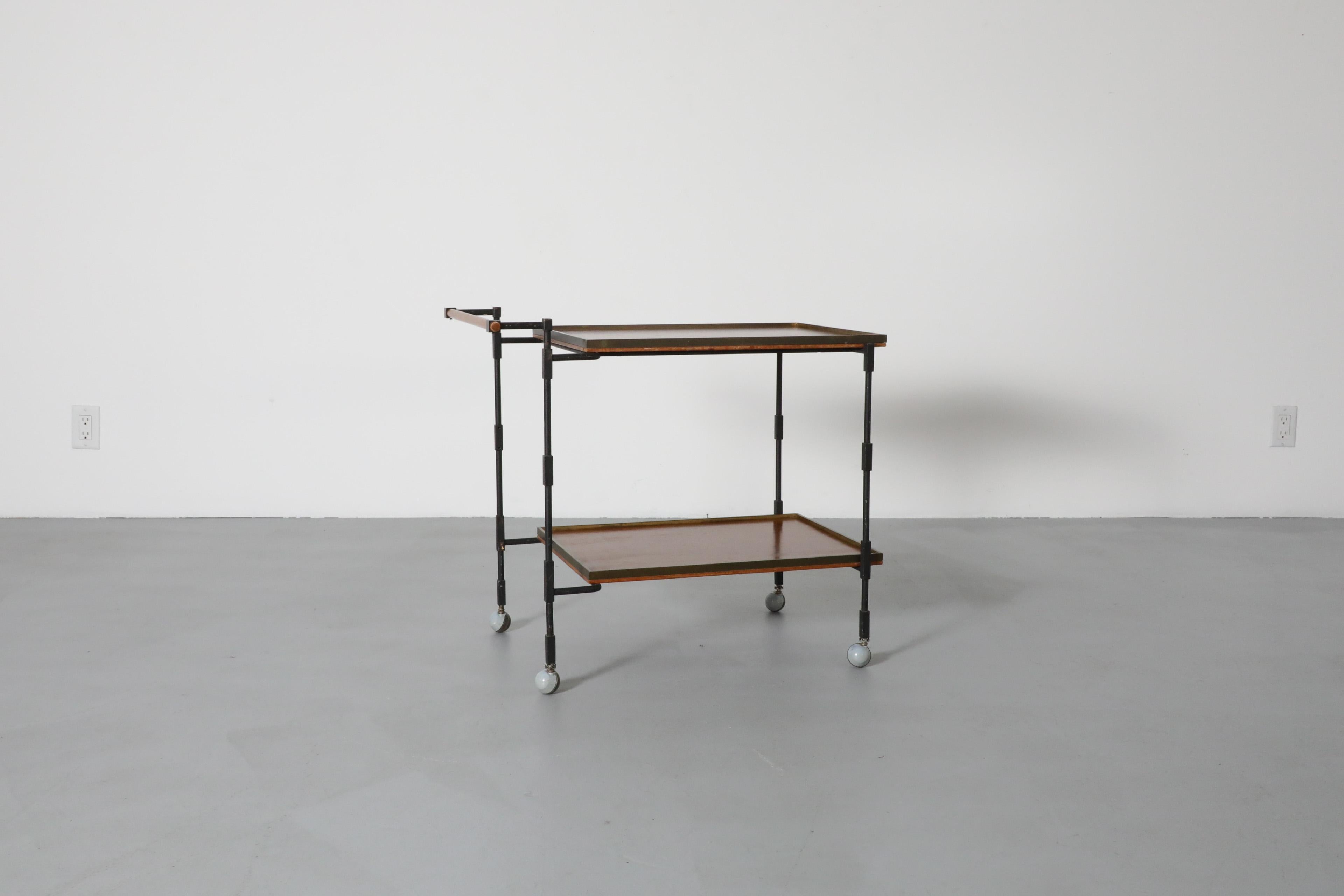 Attractive Ilse Möbel Modernist teak, iron, and brass rolling bar or service cart with wood handle. Upper and lower shelves elegantly framed in brass. Black painted iron rod frame with rectangular joints throughout. Brass and light gray round