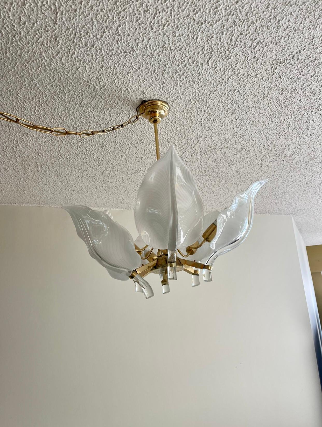  A vintage Italian chandelier, with six curled white Murano glass leaves, rendered through Sommerso technique, set in holders joined to a brass frame, suspended by a rod and circular disc canopy. Requires nine bulbs. Good vintage condition with some