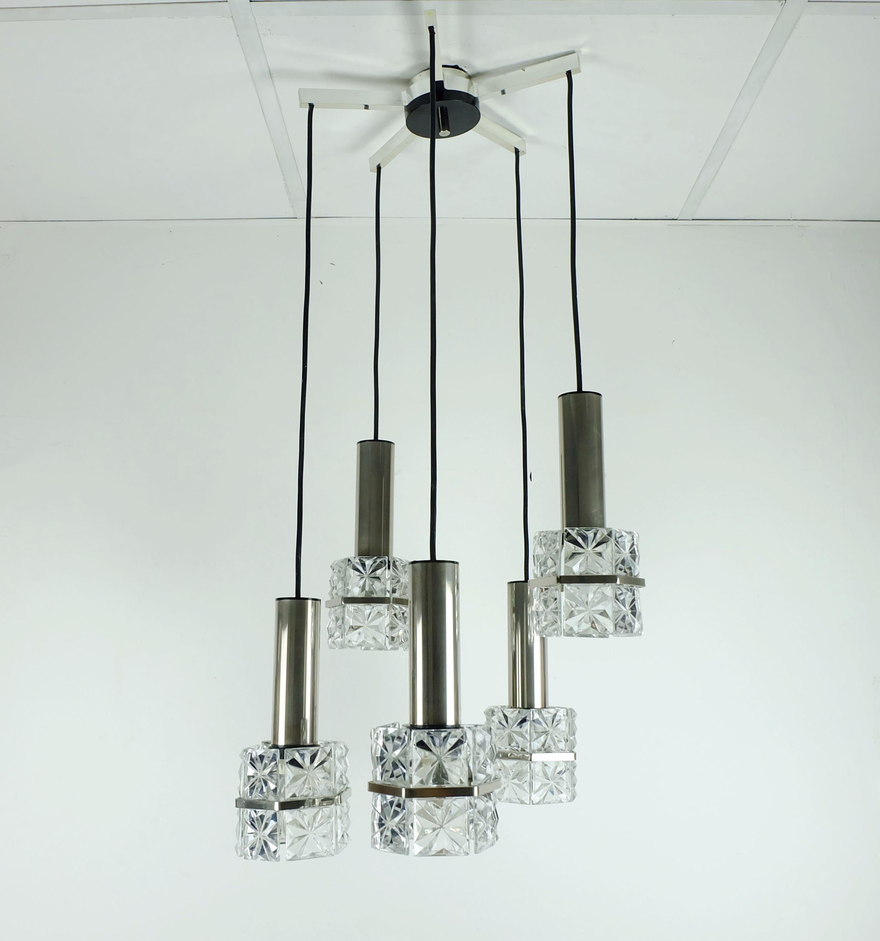 Bellissima lampada a sospensione a 5 luci della metà del secolo scorso. I paralumi sono costituiti da elementi in cristallo sfaccettato fissati su basi in metallo cromato. Fili elettrici neri. La parte superiore è realizzata in plastica nera e