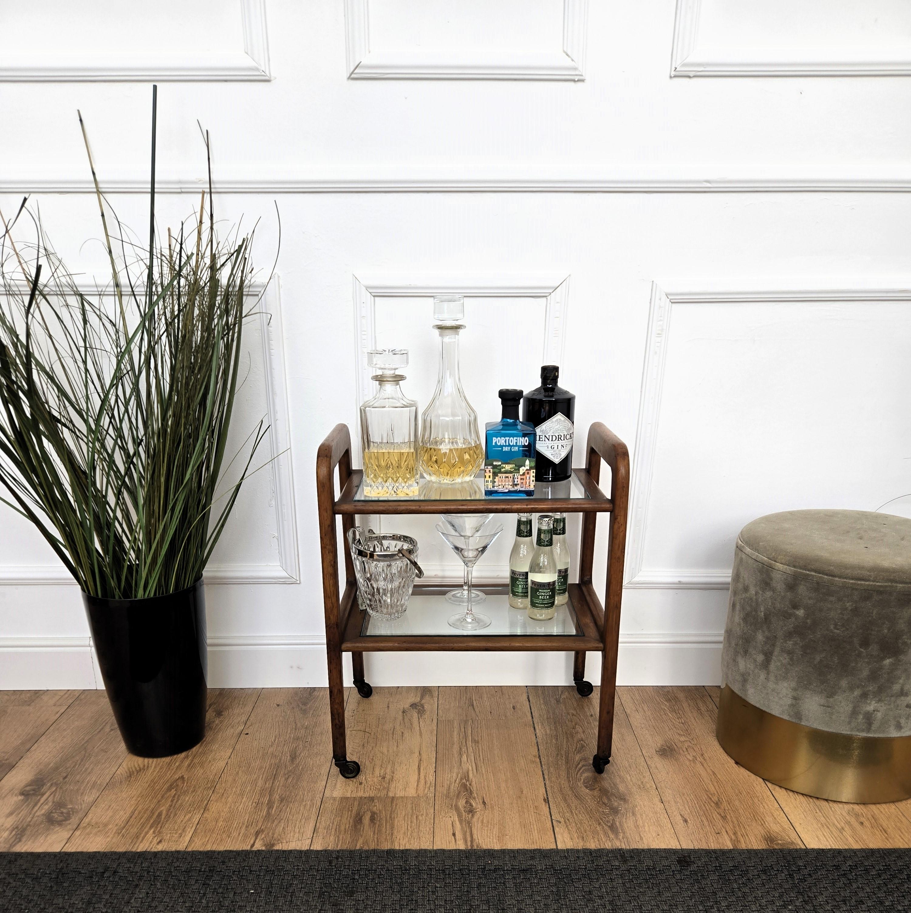 Unique and very elegant Italian Art Deco Mid-Century small cart ideal as dry bar cabinet with two glass tiers and highlighted by the great wooden structure design and overall shape completed by the original antique brass wheels. 