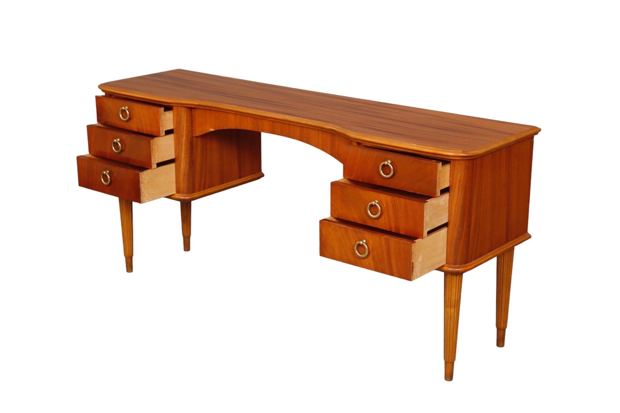 A 1960’s mid century desk that could also be used as a vanity. Six dovetailed drawers that open with round brass pulls are decorated with crotch mahogany veneers. The frame is made of teak with rich grain and round tapered legs are