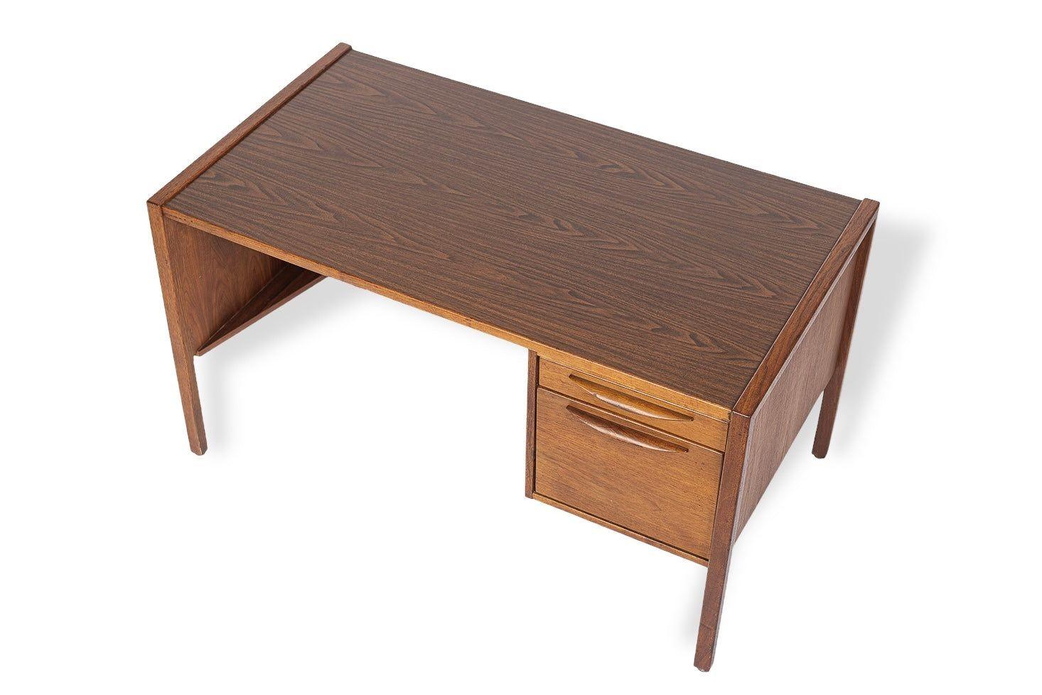 This vintage mid century modern desk by Jens Risom and circa 1960 has a classic Danish modern design with clean, minimalist, geometric lines. The desk is well-crafted heavy, and features a solid walnut wood frame with laminate top and back. The