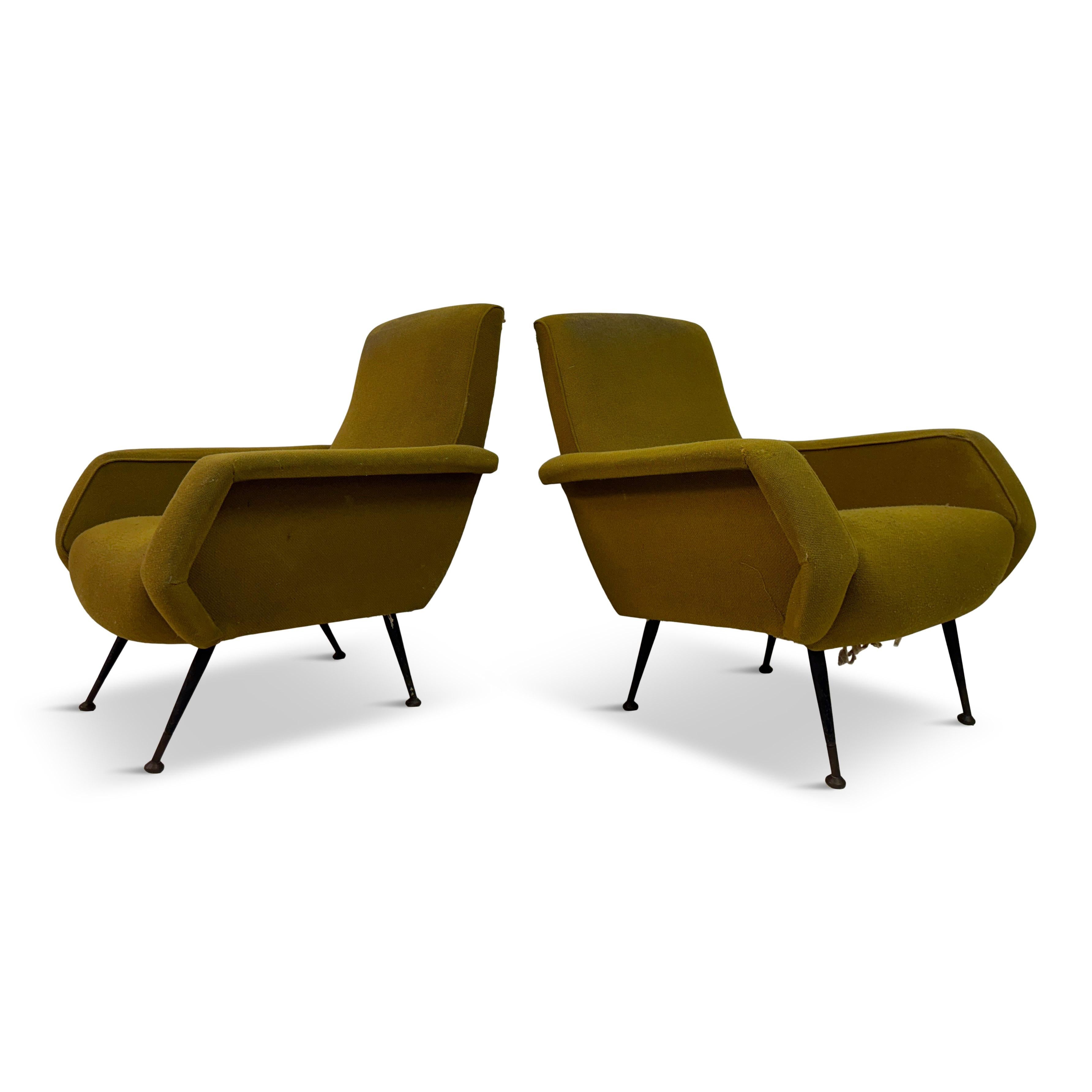 A pair of 1960s armchairs, characterized by their distinct mid-century modern design. The chairs are upholstered in a mustard yellow fabric, which shows signs of wear, indicative of their age and use over the decades. The upholstery has a slightly