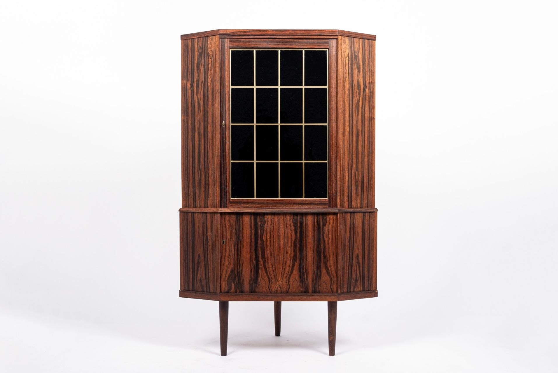 This vintage midcentury Danish modern rosewood corner bar cabinet is circa 1960. The Classic, Minimalist Scandinavian design has clean elegant lines and is well-crafted from rosewood with beautiful natural grain. The cabinet features a large tinted
