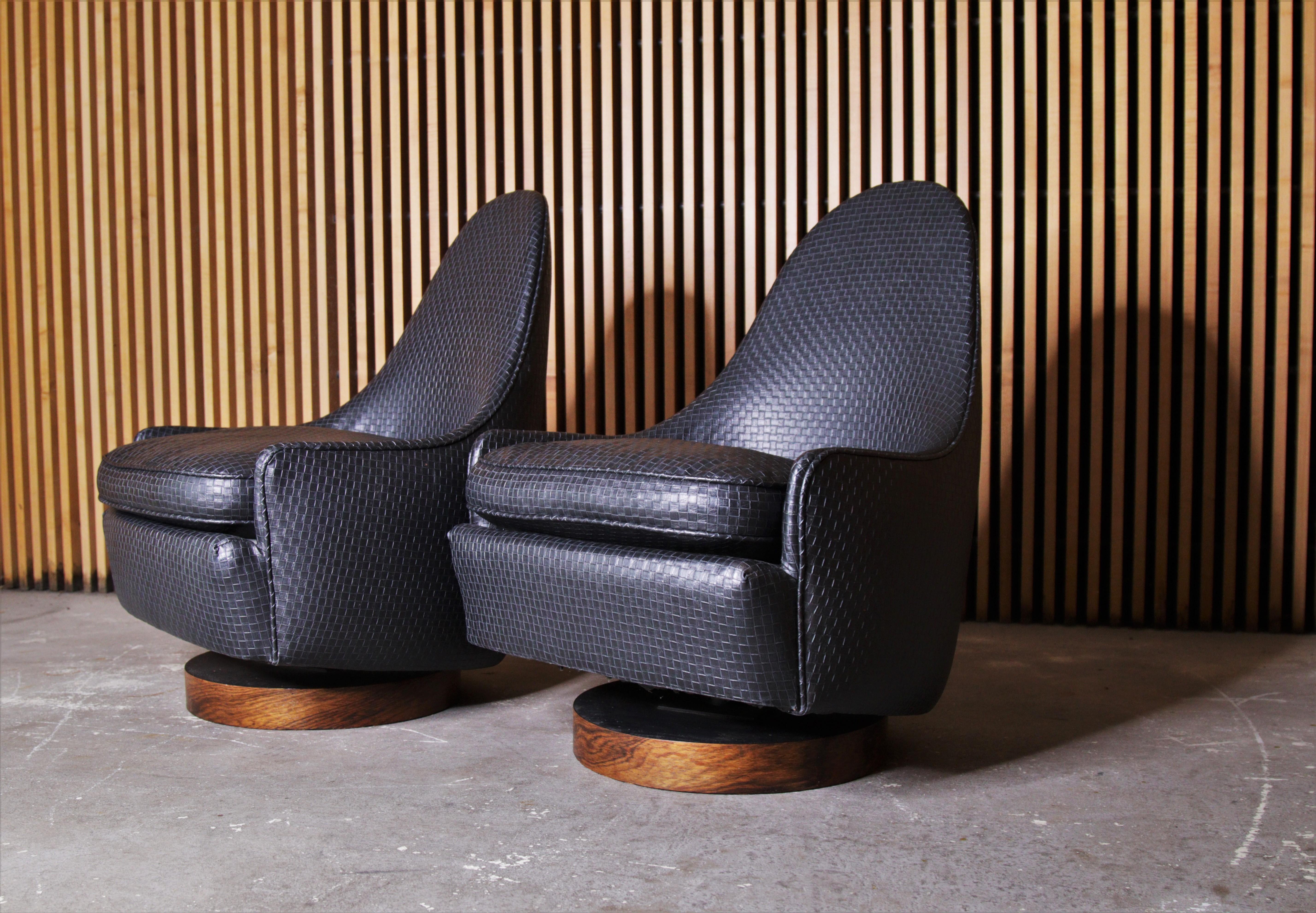 A pair of petite swivel and rocking teardrop lounge chairs designed by Milo Baughman and manufactured by Thayer Coggin. These examples with rosewood veneer bases and a woven black leatherette. 

Dimensions:
28
