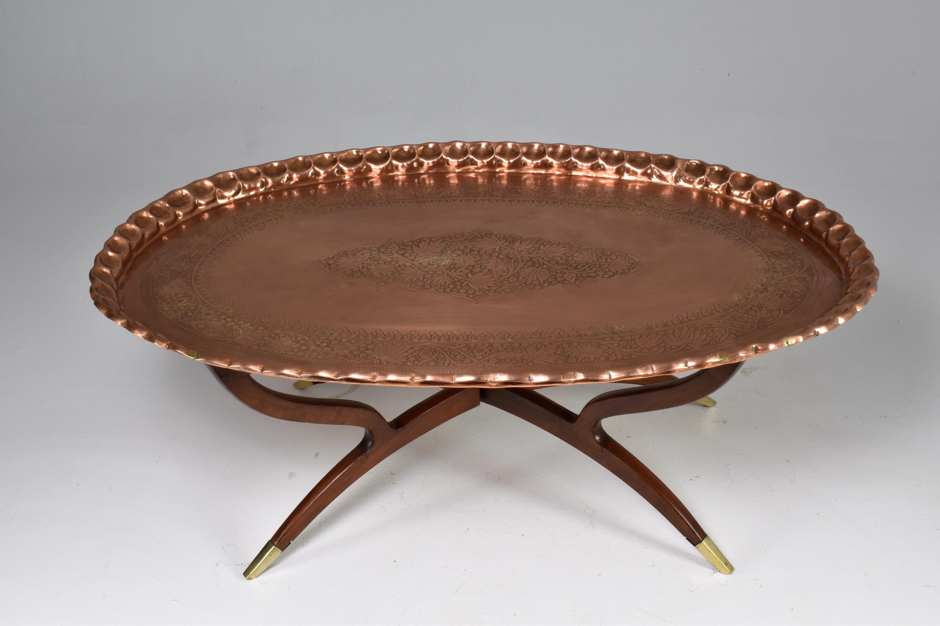 A fantastic 20th mid-century vintage Moorish oval-shaped coffee table composed of a removable meticulously sculpted and hand-engraved copper tabletop and a sculpted foldable wooden base with beautiful brass endings. A great work of Moroccan