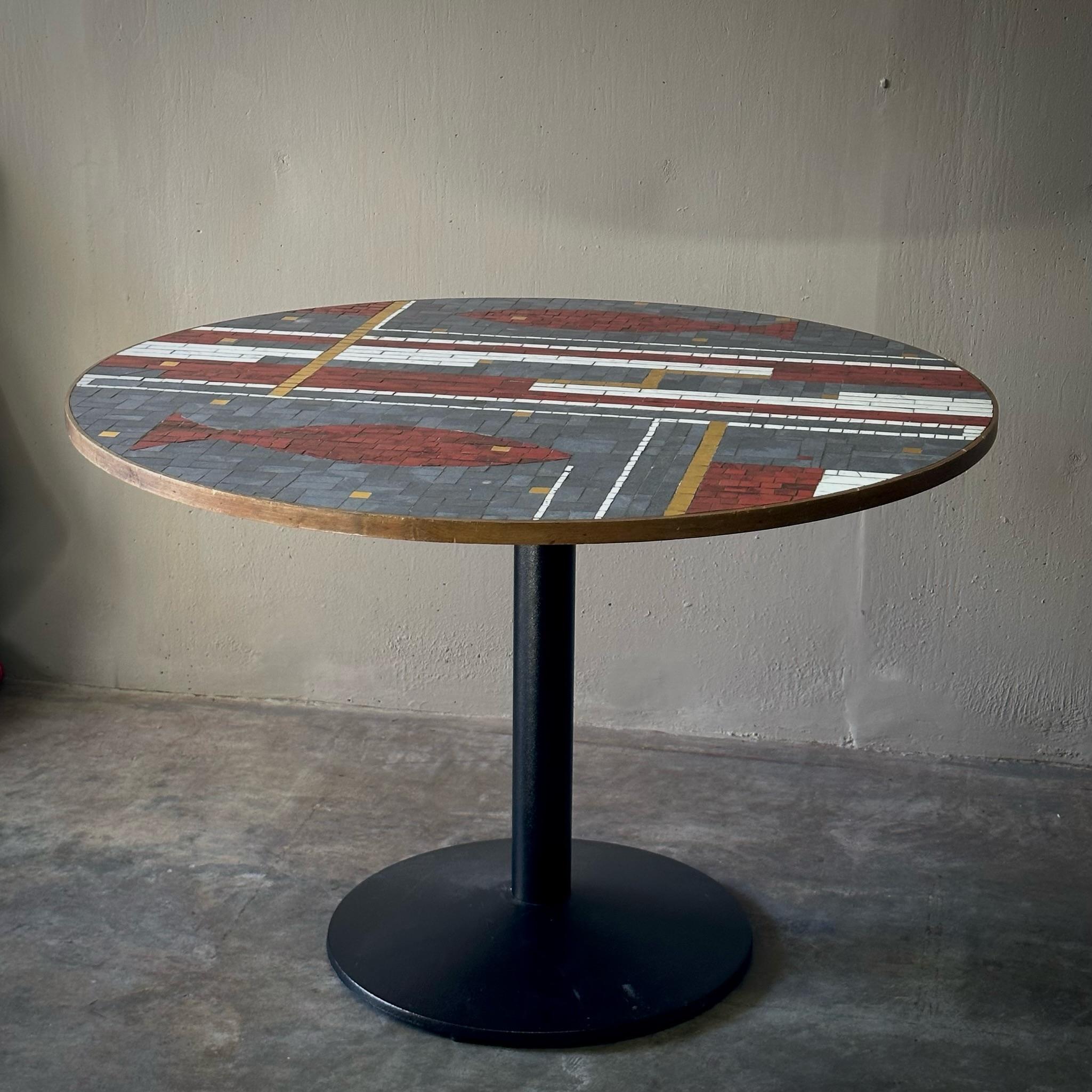 Whimsical 1960s Dutch circular mosaic table featuring graphic Mondrian-like design with fish motif in tiles of gray, red, yellow, and white. Mounted on a simple industrial iron pedestal base, this unique midcentury dining or center table would work