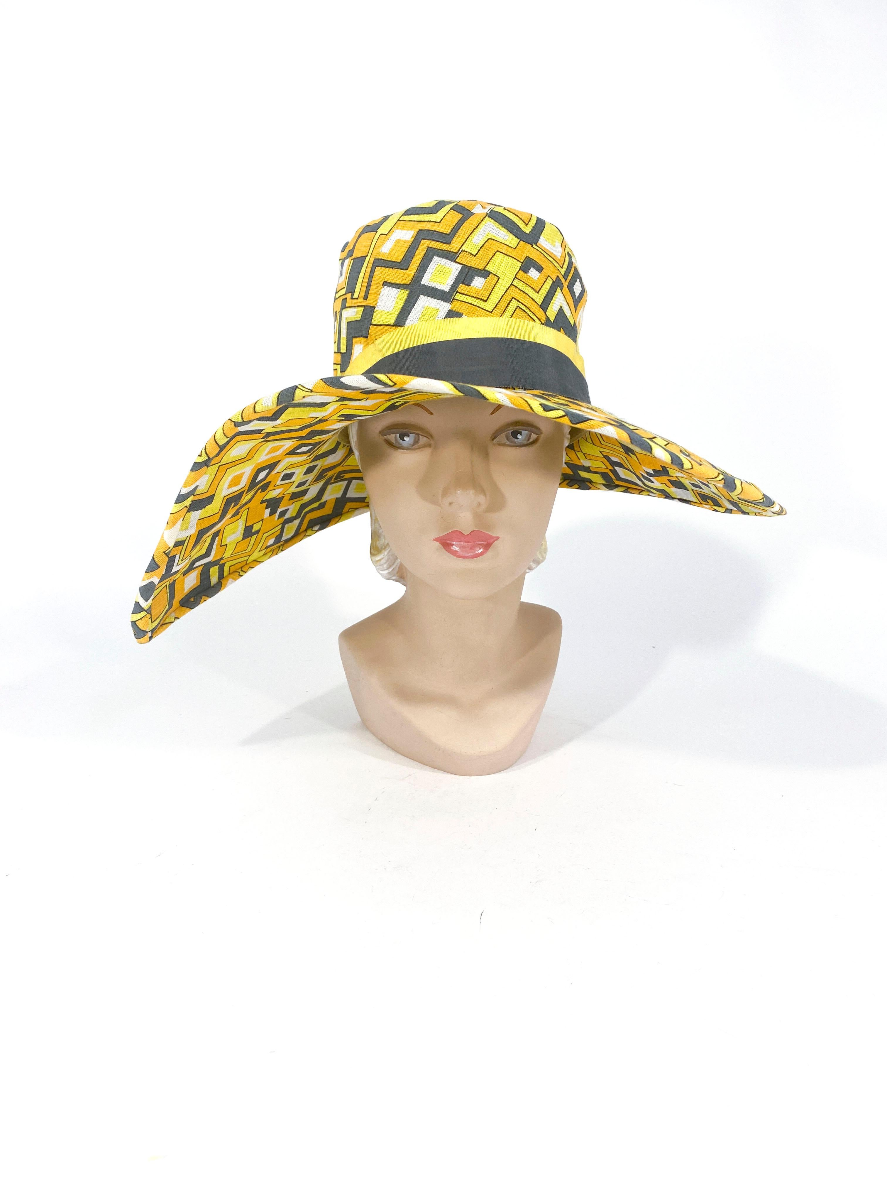 1960s in a 1920s style Mr. John Geometric printed hat with a wide asymmetrical brim. The print features yellow, white, grey , and gold. The hat band is two-toned in yellow and grey grosgrain ribbon accented with grey decorative buttons.