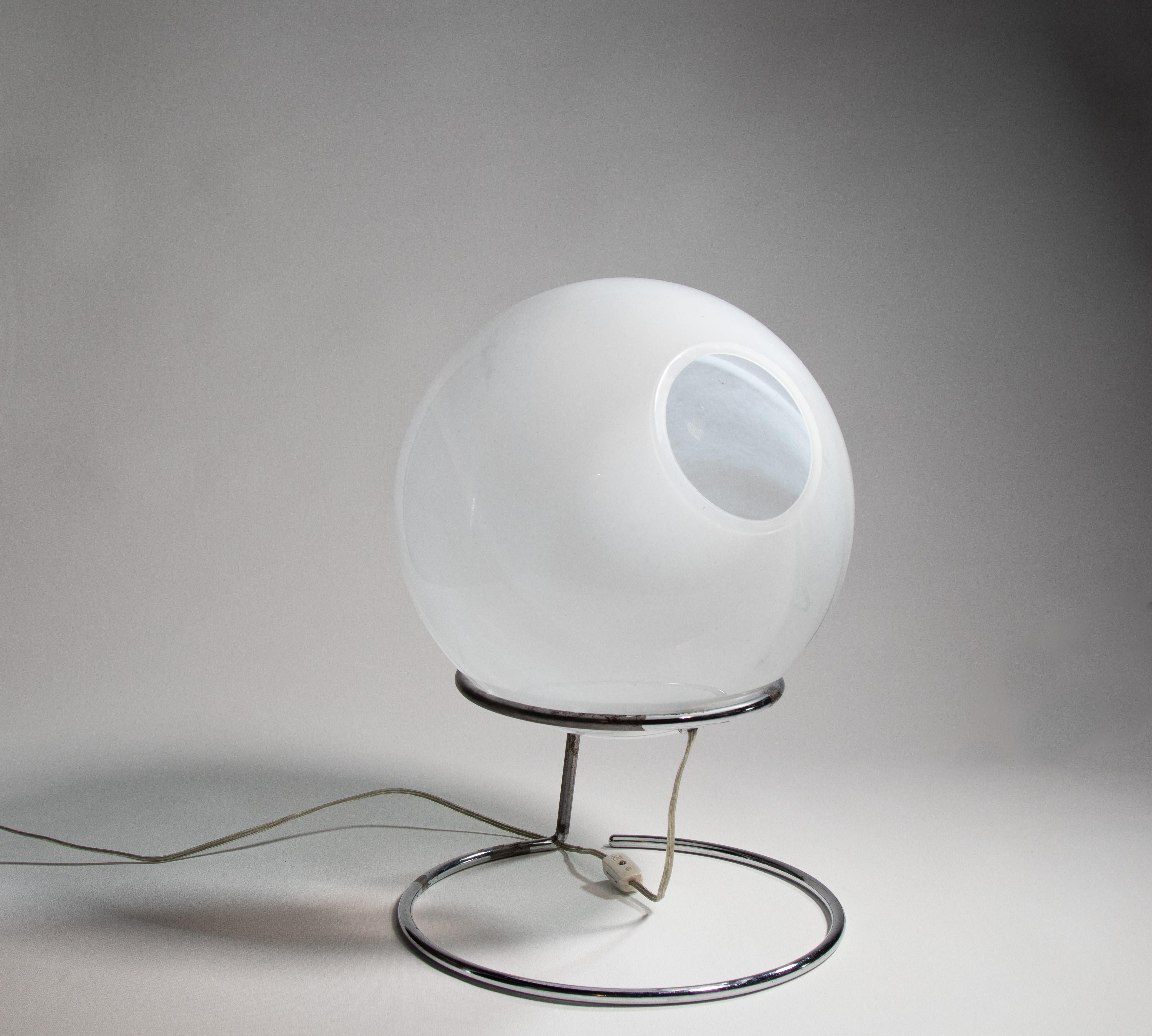 A unique lamp featuring white swirled art glass cantilevered over a chrome floating stand. The eye can be adjusted to focus light on an object while allowing a warm overall glow. The glass orb rests freely in the chrome stand. 

Dimensions:

12”