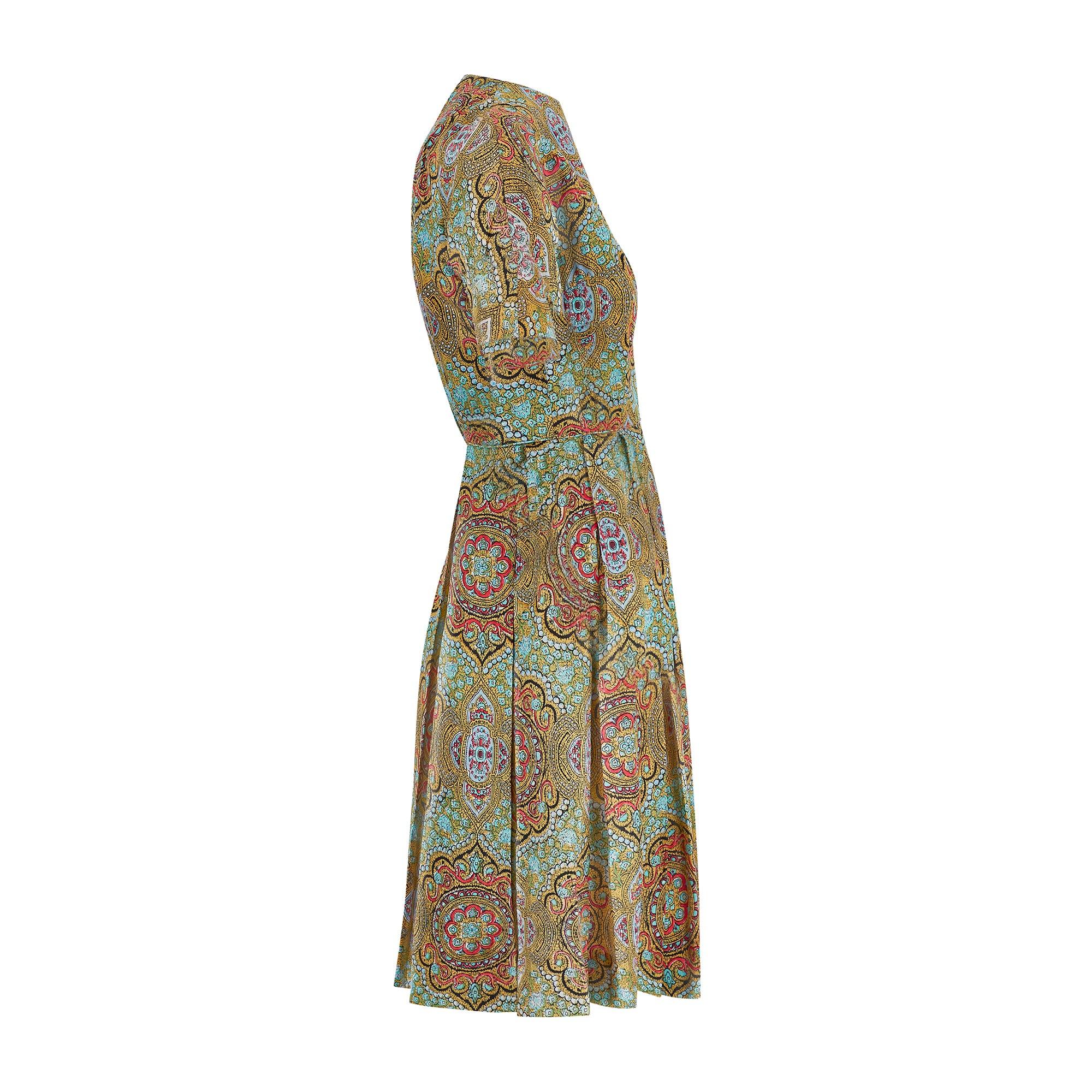 Este vestido atemporal de seda de los años 60 está confeccionado en seda suave y estampado por toda la prenda con un diseño paisley clásico actualizado para la época en vibrantes tonos mostaza, aguamarina y rojo coral. Tiene mangas cortas y cintura