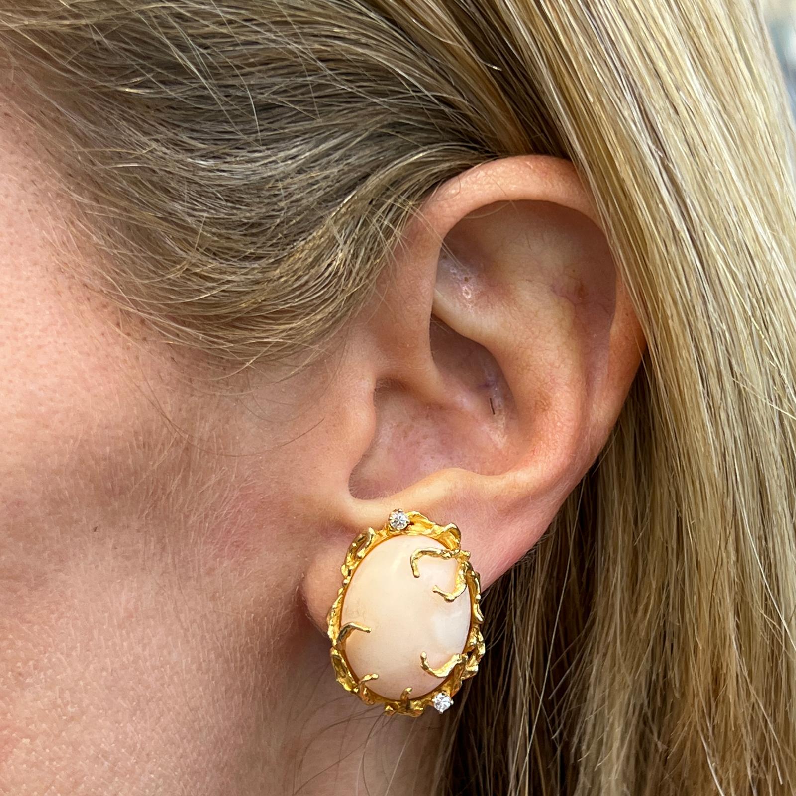 Angel skin coral and diamond earrings crafted in 14 karat yellow gold. The earrings feature two natural oval cabochon coral skin angel gemstones set in free form yellow gold with 4 round brilliant diamonds accents weighing .20 carat total weight.