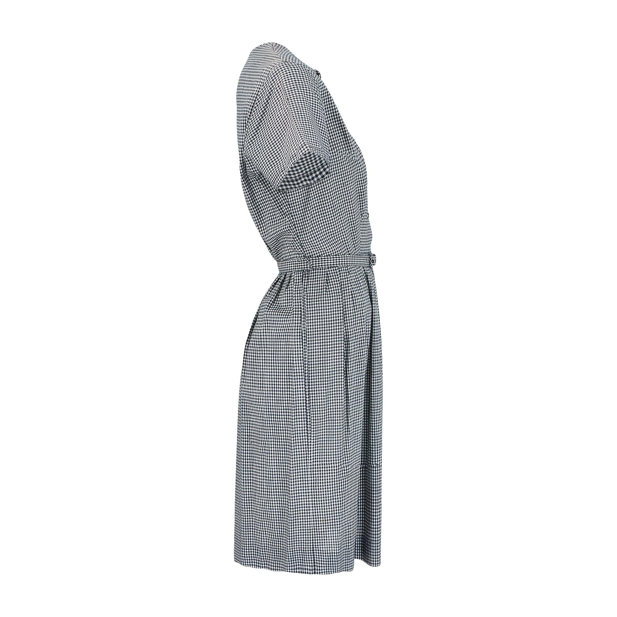This midnight blue and white gingham cotton dress was made in the USA in the late 1950s to 1960s by an unknown designer.  A desirable shirtwaister style which falls to just below the knee, it is full-skirted and pleated, typical hallmarks of dresses