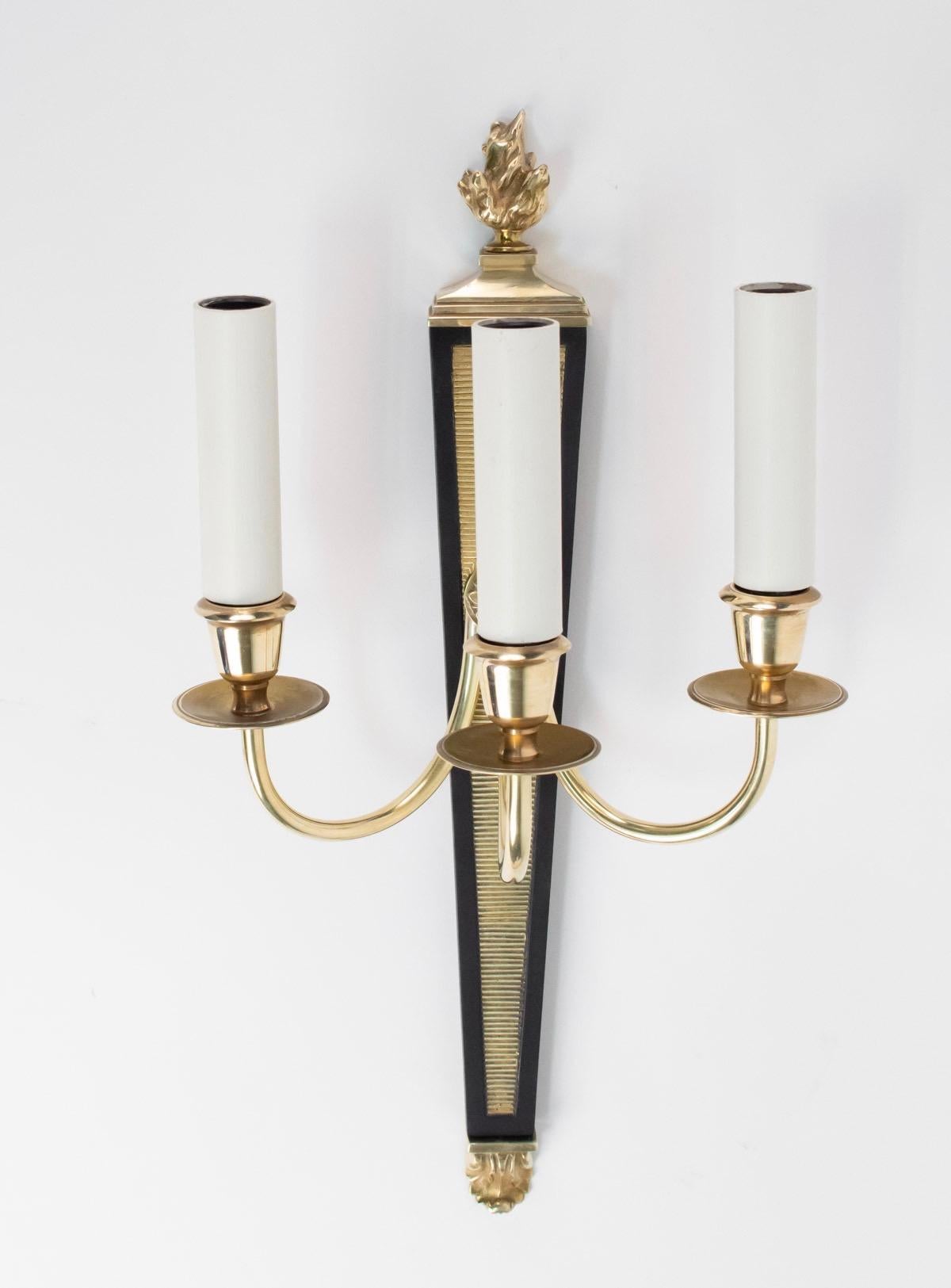 Elegant pair of Maison Charles sconces, France, 1960s.
Trapezoidal back plate made of blackened bronze adorned with fluted gilded bronze piece. The both extremities are ended stylized flames.
The three arms are made of brass and ended with a