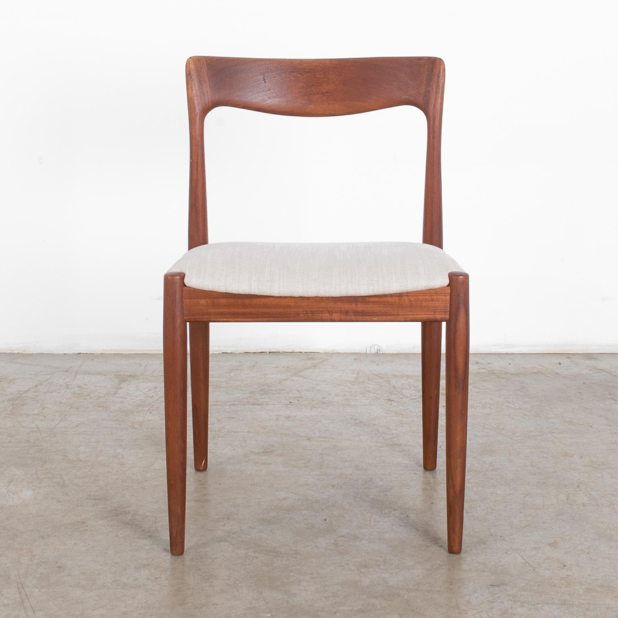 A 1960s teak chair by Danish furniture designer Neils O. Møller. A modernist design with tapered legs and fluid, expressive back piece. A cushioned seat is upholstered in a natural white. The warm, rosy tones of the teak emphasize the sophistication