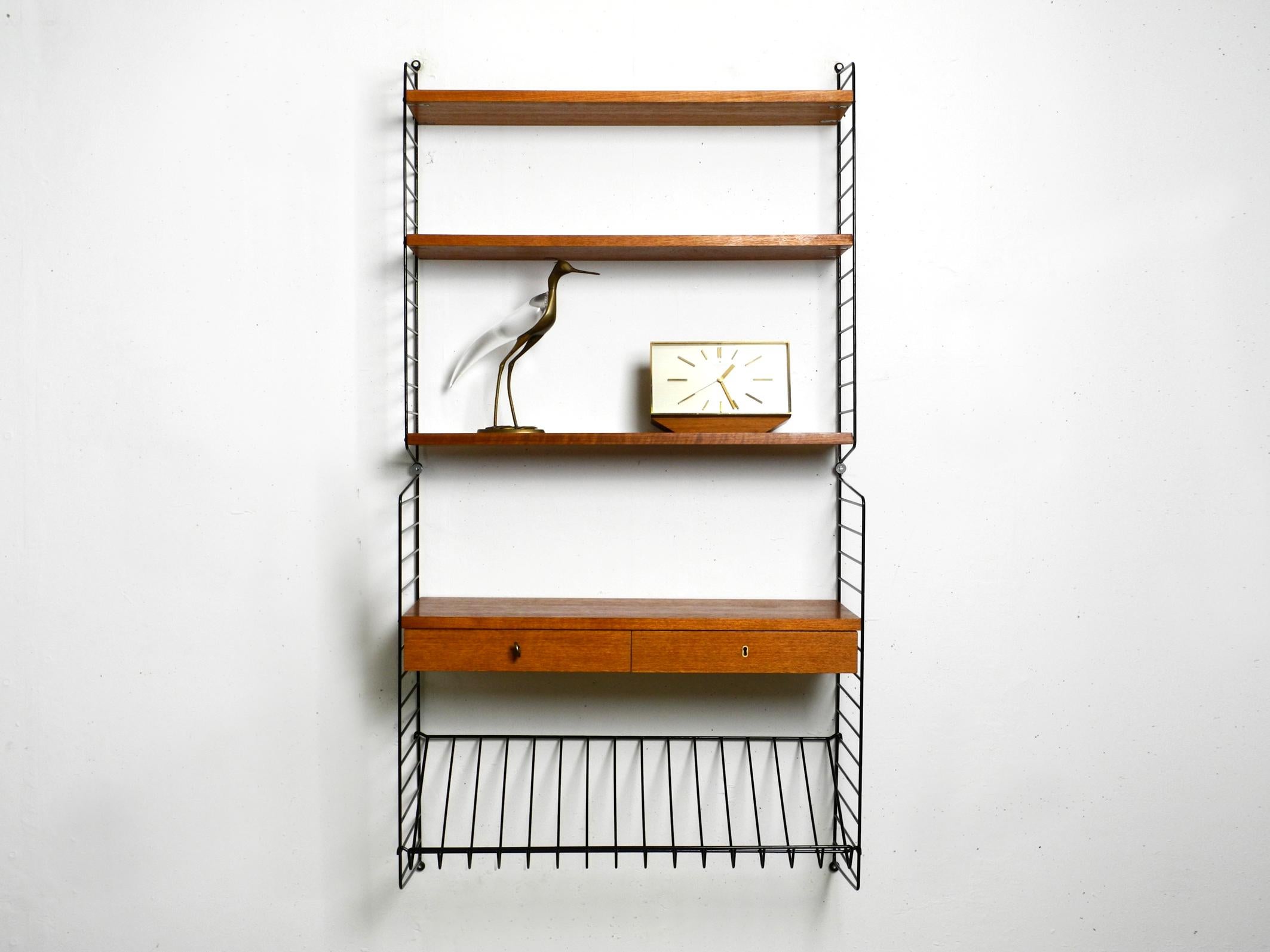 Original 1960s Nisse Strinning String teak wall shelf with a depth of 20 cm and 30cm.
Made in Denmark. With one original brass key. Locks both drawers.
Two ladders with three boards 20 cm deep. Two ladders with a depth of 30 cm shelves and two