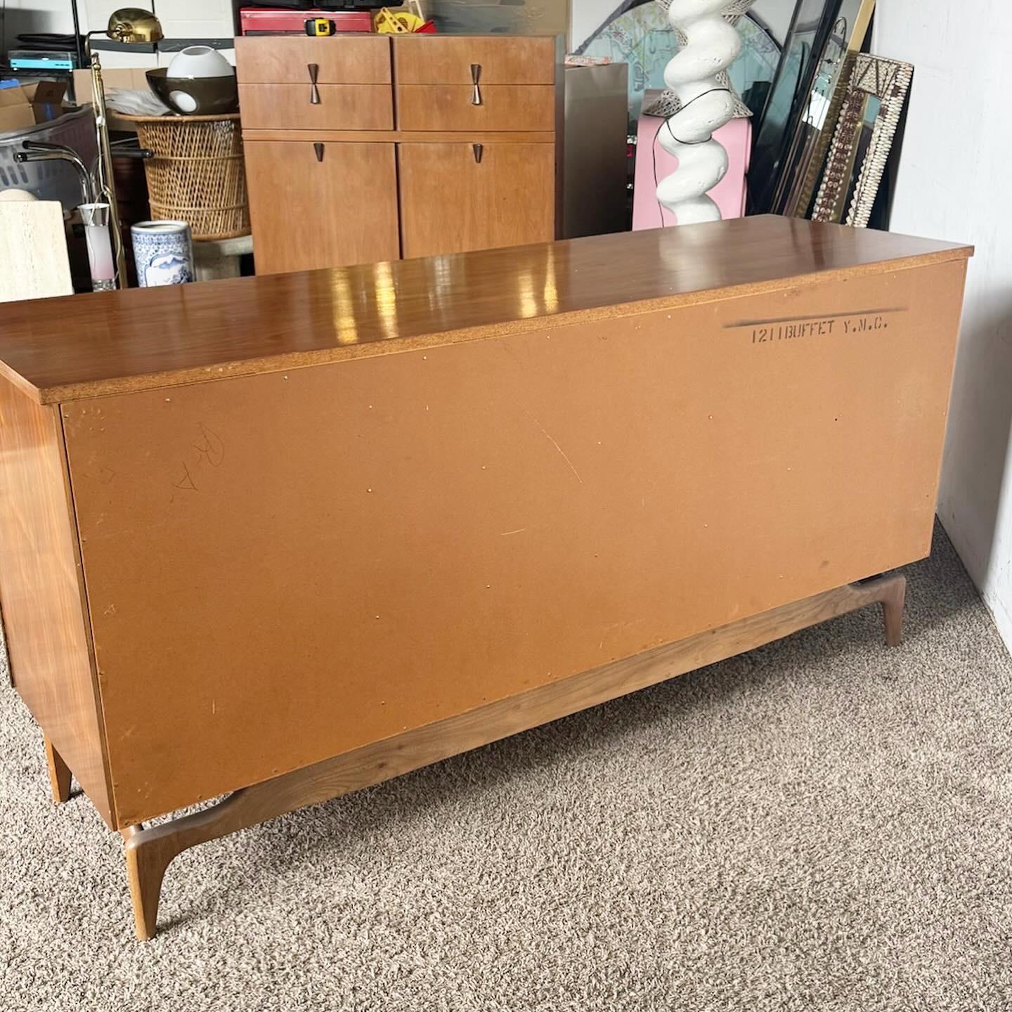 The 1960s North American Mid Century Modern Walnut Credenza is a timeless piece, embodying mid-century design. Crafted with durable walnut, it features sculpted drawer pulls and ample storage. This credenza stands on four elegant legs, perfect for