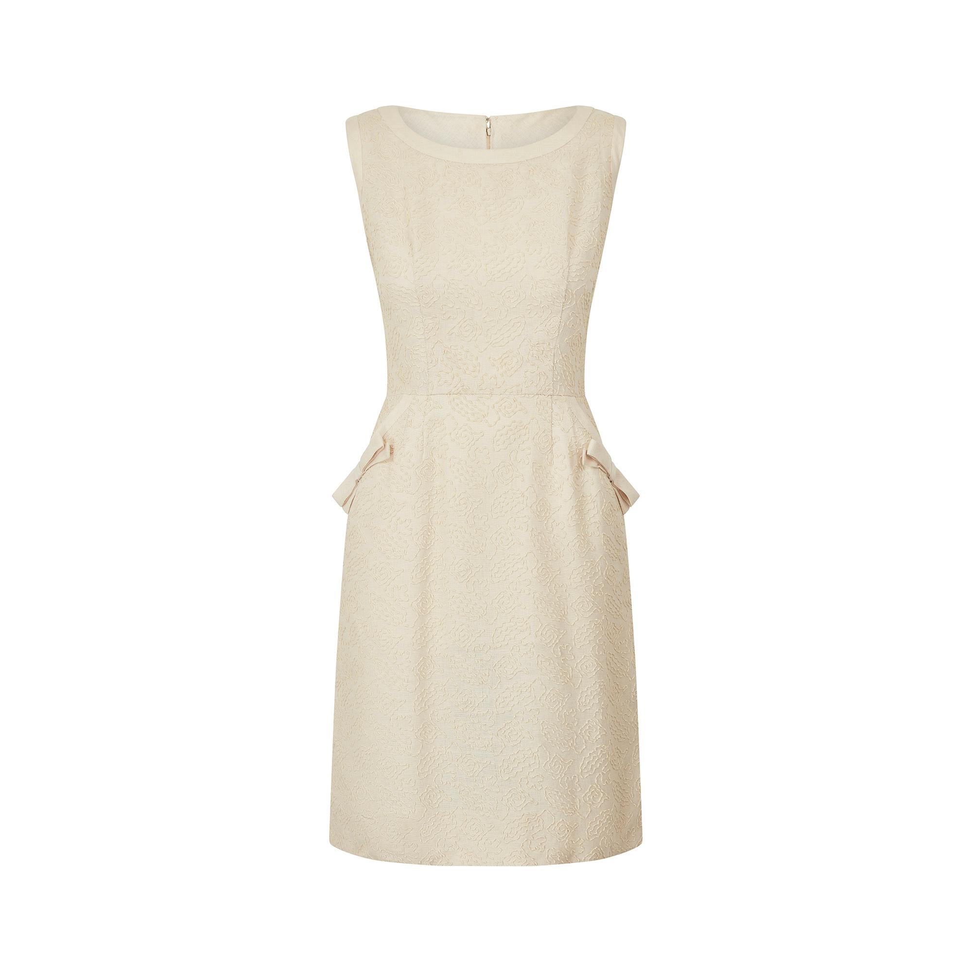 This is a beautifully finished 1960s textured linen work dress in a light cream oatmeal shade. It tapers from the bust to the waist in a classic 60s shift shape and flows down into a pencil silhouette. The rounded neckline and shoulder straps are
