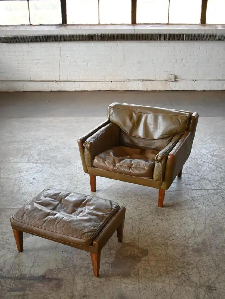 Fantastic leather chair with ottoman in olive brown buffalo leather raised on rosewood legs. This rare model which resembles the fabled model V11 was designed by Illum Wikkelsø and manufactured by Holger Christiansen in Denmark in the 1960s. Low and