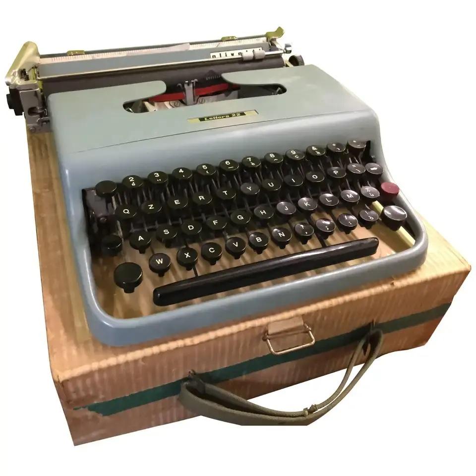 For sale is a charming early edition Olivetti Lettera 22 typewriter, featuring round characters and accompanied by its original paper box. This vintage typewriter showcases a light pale green/blue color, with slight discoloration due to its age,