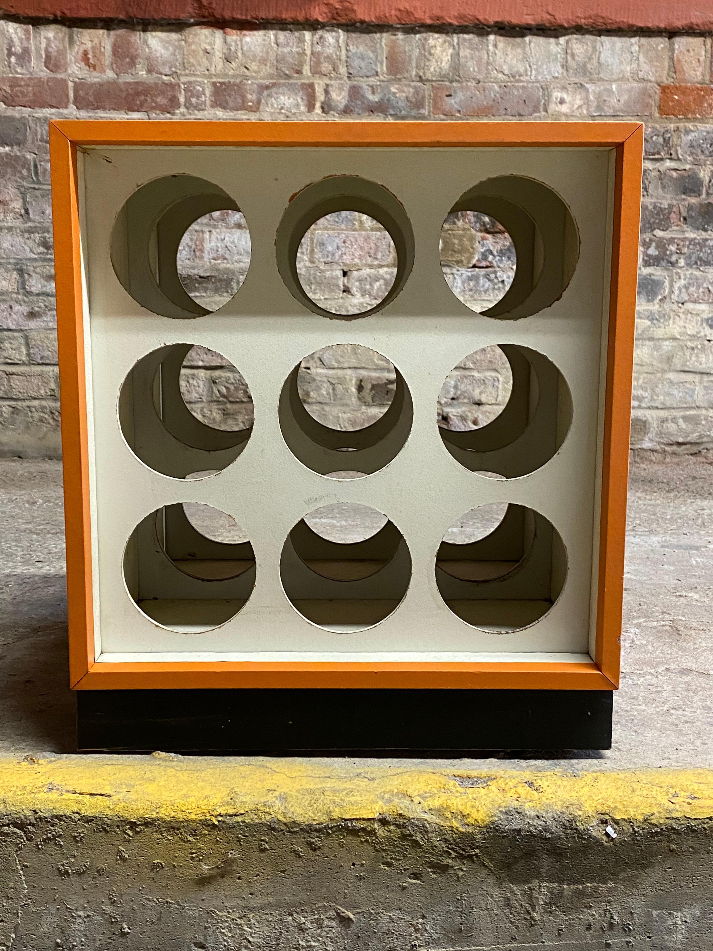 A fun color pop wine rack/side table. Orange vinyl clad cube with an 18 hole masonite inserts on two sides. Black base. Good overall condition with some minor nicks to the vinyl. Minor scuffs and light scratches. Structurally sound and sturdy. Some