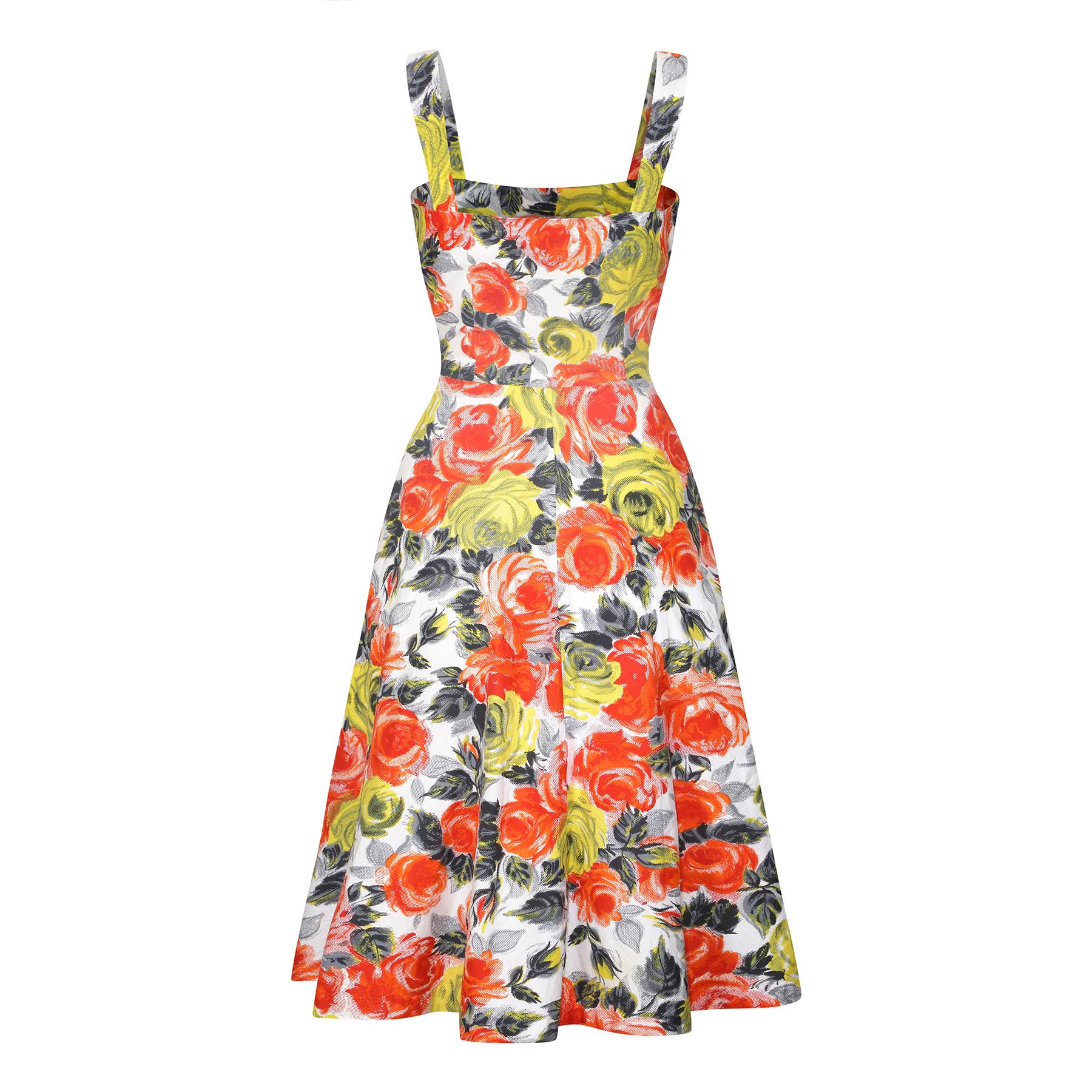 Se trata de un vestido estampado de rosas realmente vibrante y deseable de finales de los años 50 o principios de los 60, en una atrevida combinación de colores rojo, naranja, amarillo, gris y negro sobre fondo blanco. La impresión en sí es una