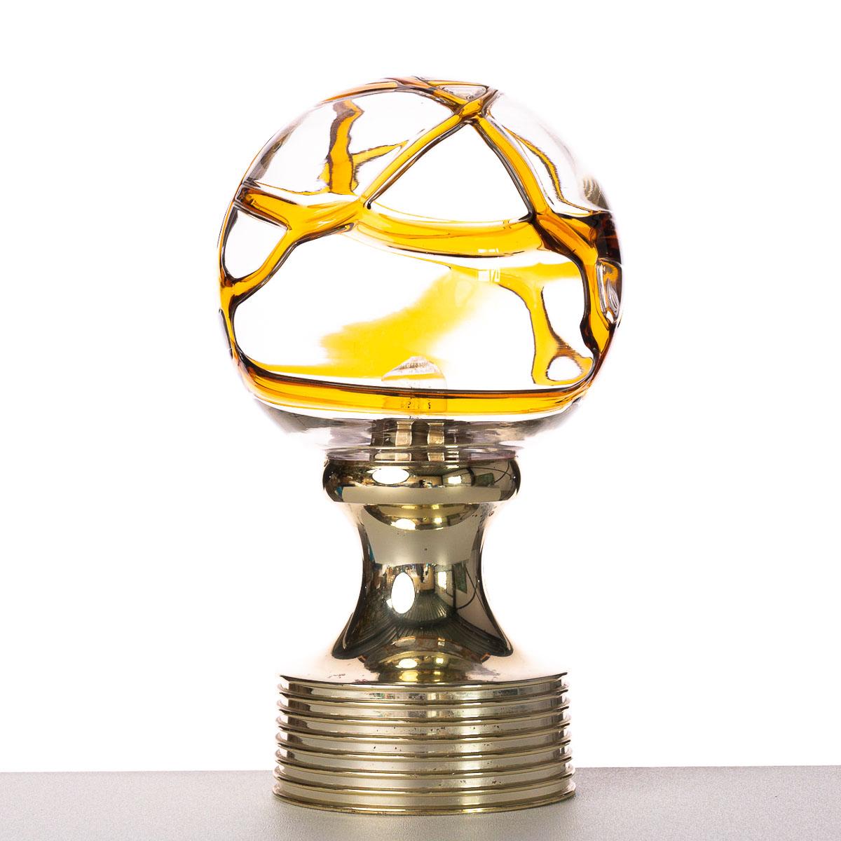 Boule en verre avec des lignes en verre jaune/orange. Pied en plastique avec couche dorée. Nous avons un lustre avec une grande boule de verre avec des lignes orange similaires.