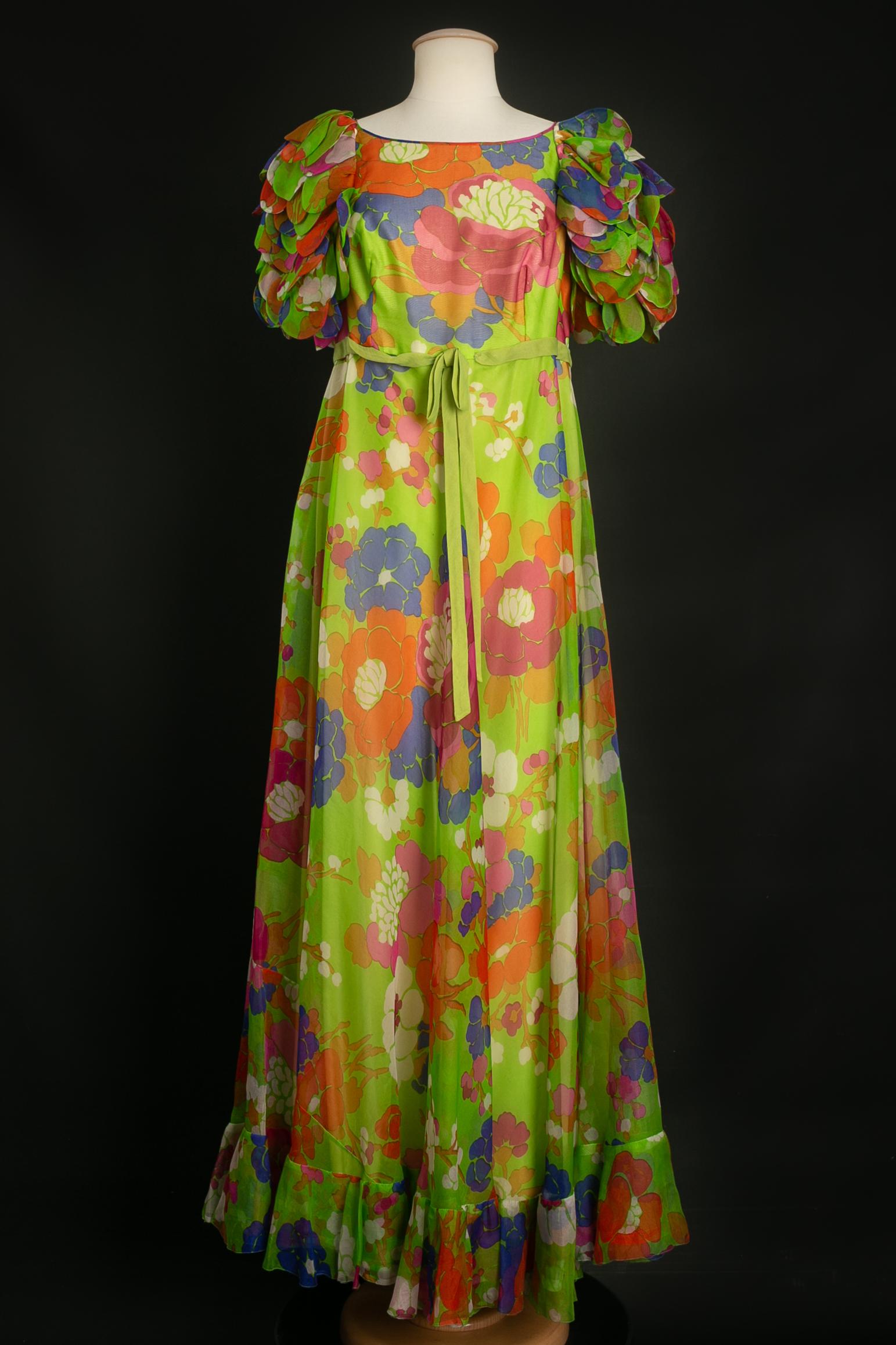 ANONYMOUS -Long dress in green organza with pink, orange and blue flowers. The short sleeves are composed of ruffles reminiscent of petals. No size or composition label present, it corresponds to a size 38FR/40FR. To note a few stains