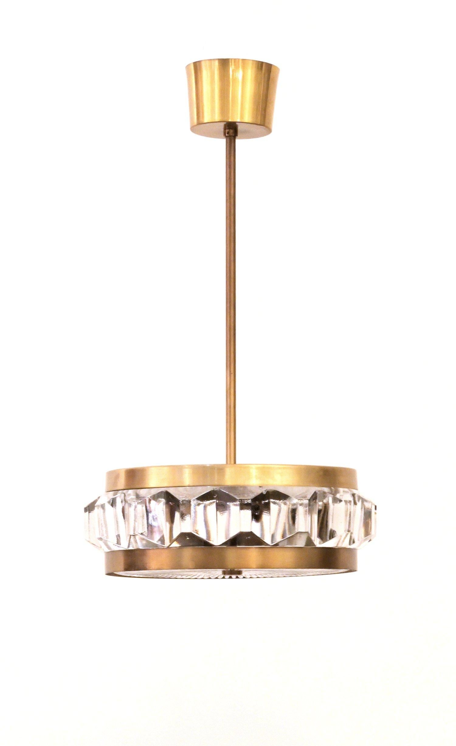 A brass pendant Orrefors light having cut geometric glass decorations in the center rim and an intricate glass detailed disc along the bottom. Contains two sockets. circa 1960s.

.