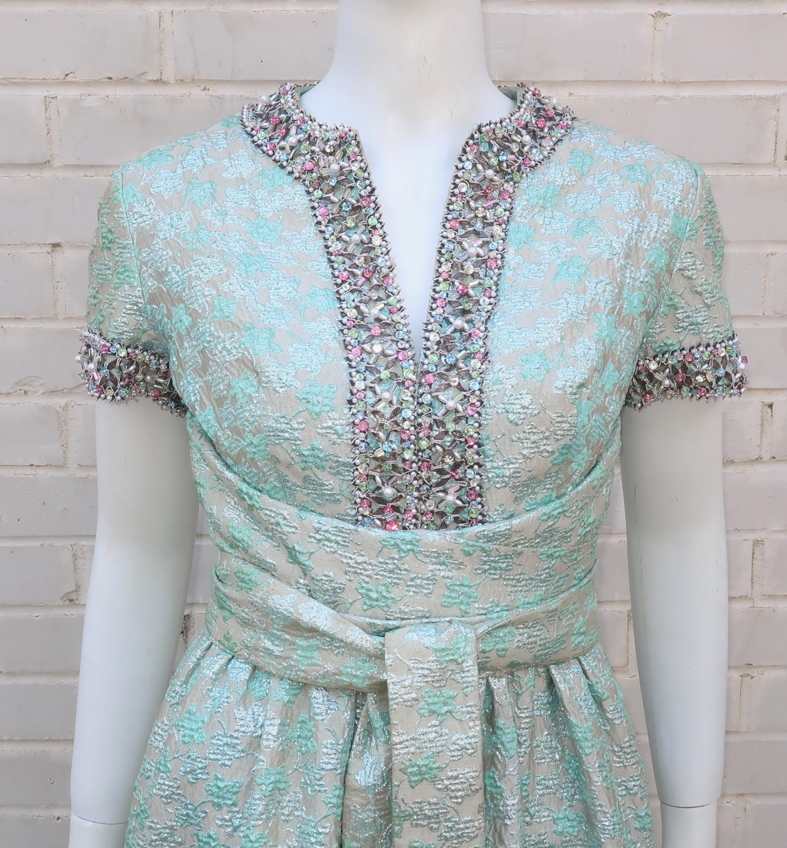 This 1968 brocade evening dress was created during Oscar de La Renta's time as head designer for Jane Derby and exemplifies his opulent style.  The silvery metallic fabric has a light background with a sea mist green floral design and is embellished