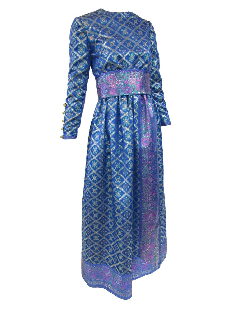 
Regal and ornate peacock colored metallic maxi dress from Oscar de la Renta. Floor length and long sleeved evening dress features a beautiful diamond print with metallic gold detailed buttons down the sleeves. Coordinating belt. Fully lined with