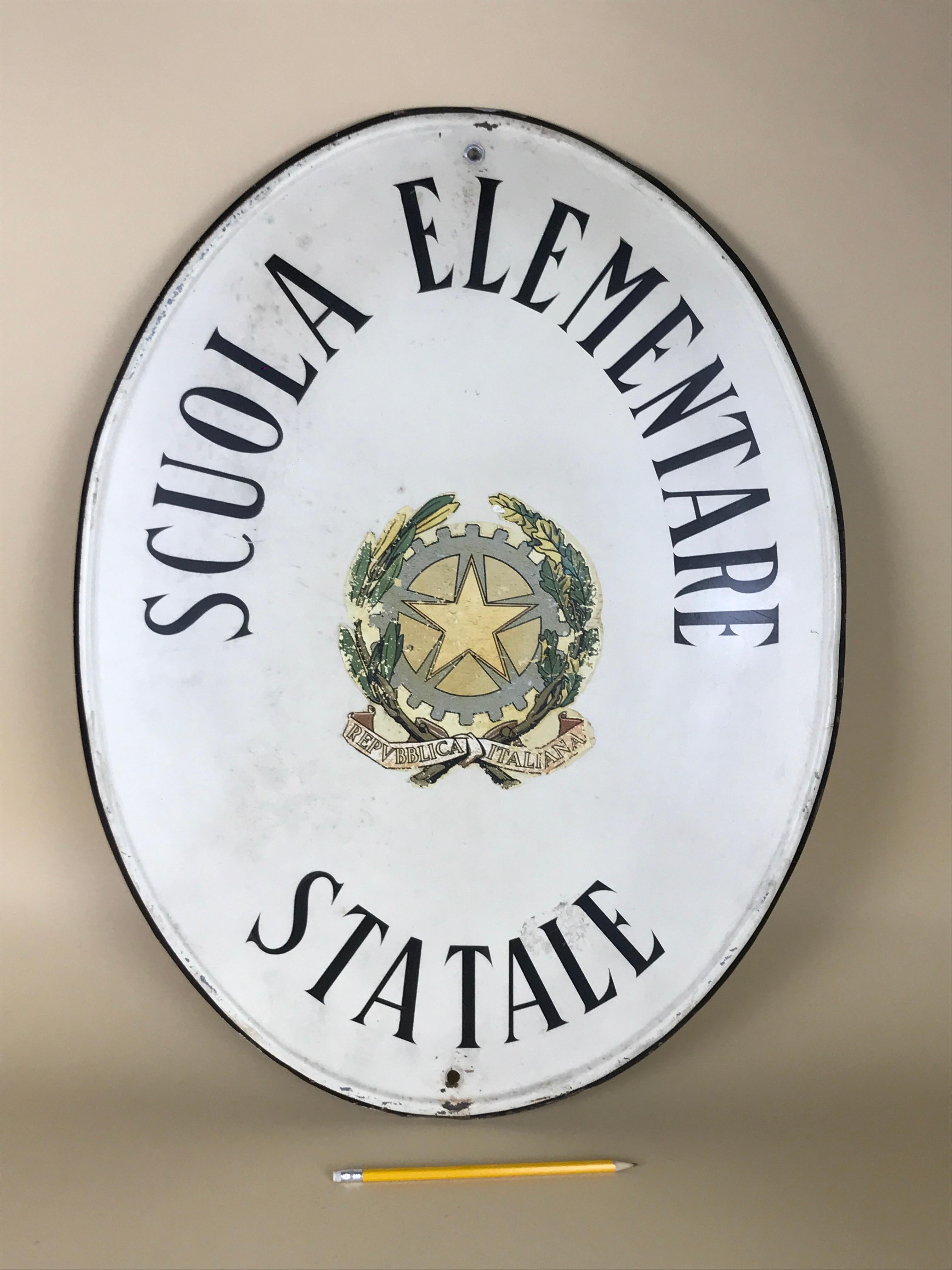 Vintage oval screen printed Italian metal sign ‘Scuola elementare statale’ or State primary school. The sign has a oval relief profile and black line profile on what is now a light cream background.
At the centre there is the very nice emblem of